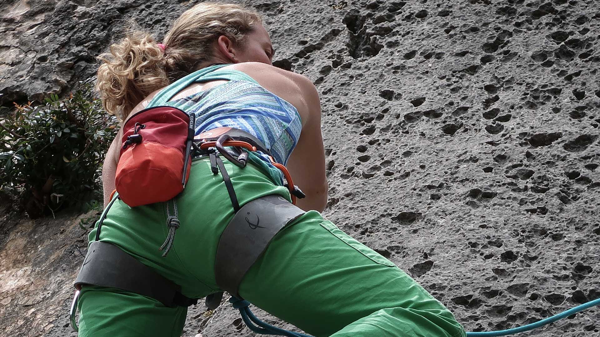 Kletterer im Vorstieg an senkrechter Felswand auf Mallorca, Klettergurt und Chalk-Bag sichtbar, Sommer.