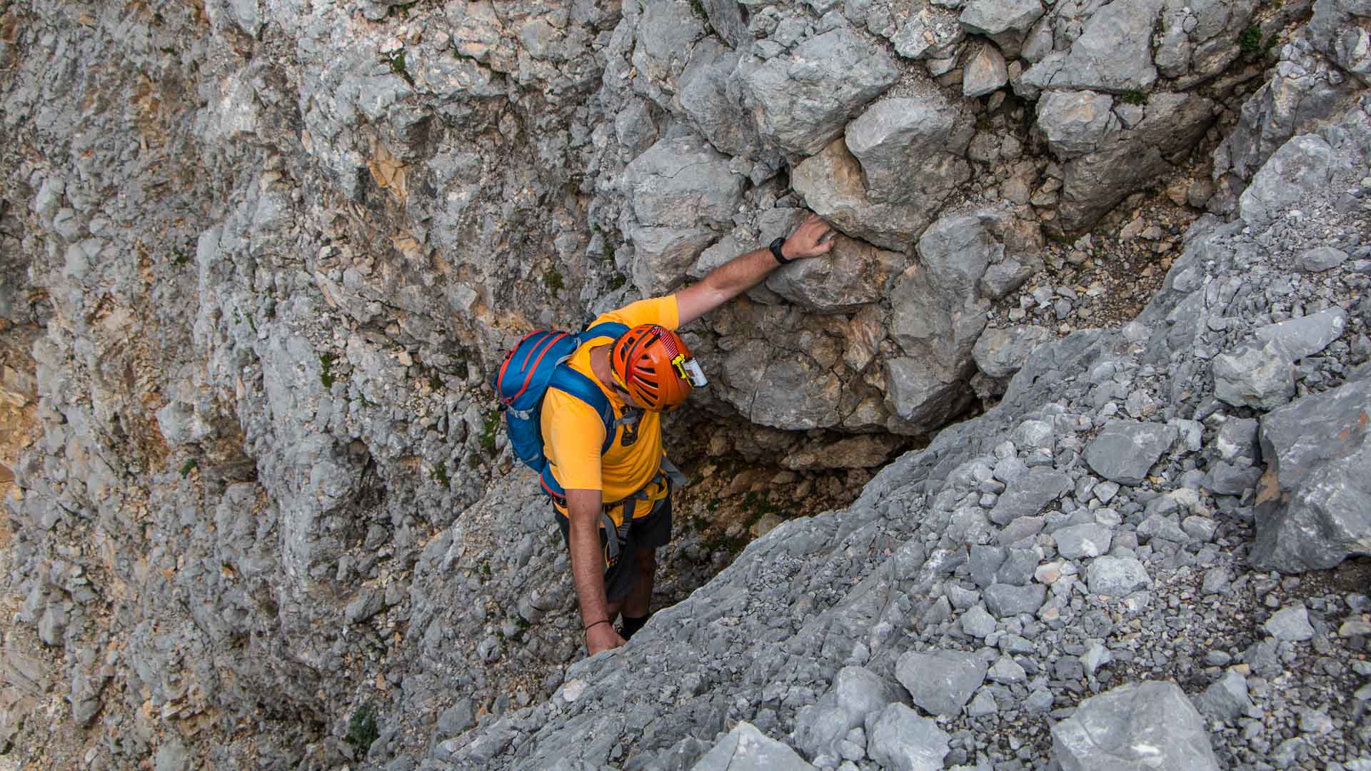 Kletterer greift an Felsvorsprung am Hochwanner, umgeben von zerklüftetem hellgrauem Kalkfels und Geröll.