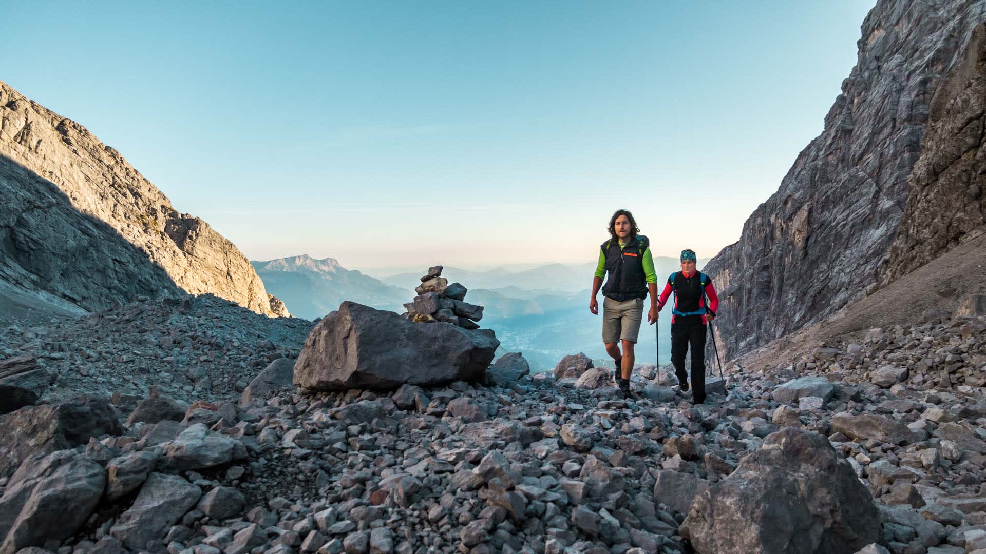 Zwei Kletterer steigen im frühen Morgenlicht durch das felsige Watzmannkar zum Einstieg der Widerroute am Watzmann auf.