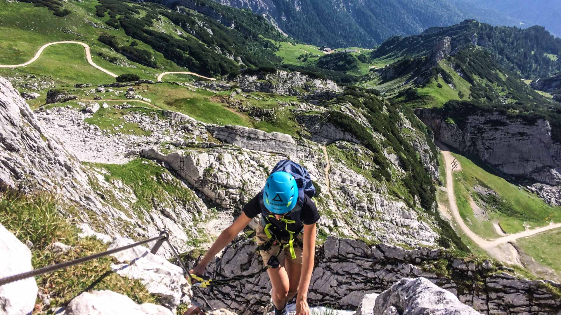 Klettersteiggeher steigt mit Helm und Rucksack an einem Fixseil der Via Ferrata zur Alpspitze auf.