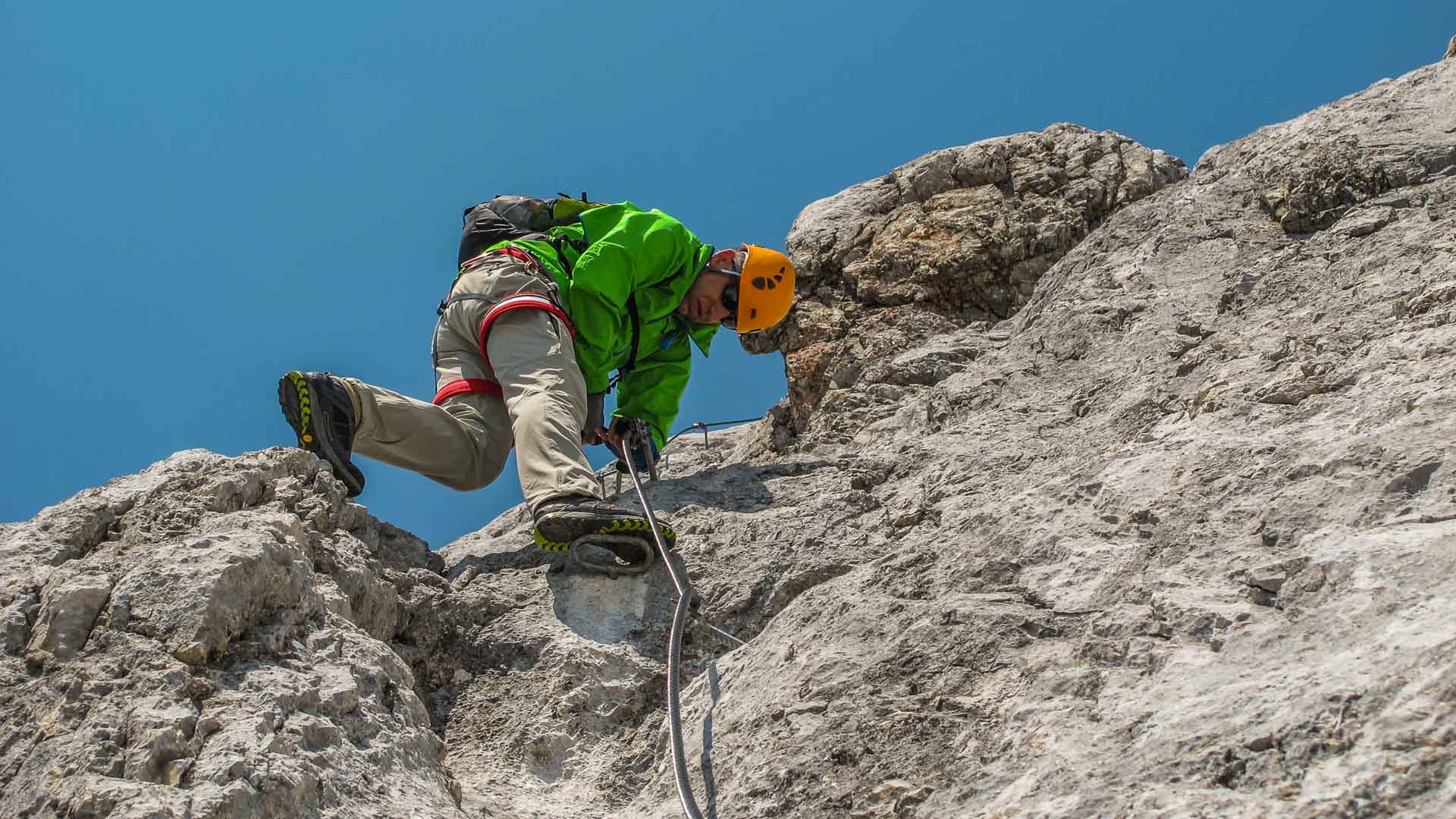 Klettersteiggeher klettert an hellem Kalkfels in Berchtesgaden, gesichert an Bohrhaken, Klettergurt sichtbar.