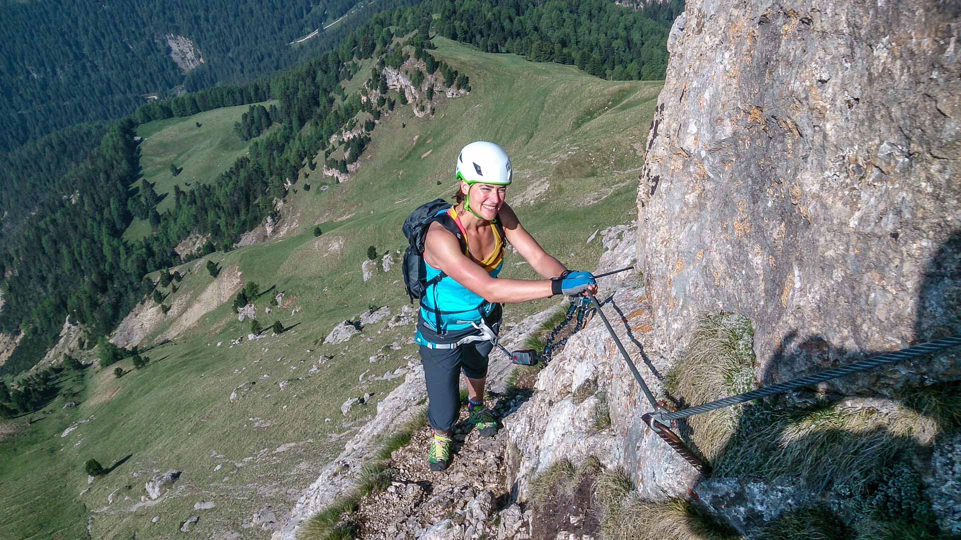 Klettersteiggeher mit Helm und Klettersteig-Set am Stahldrahtseil in den Dolomiten, Tal im Hintergrund.