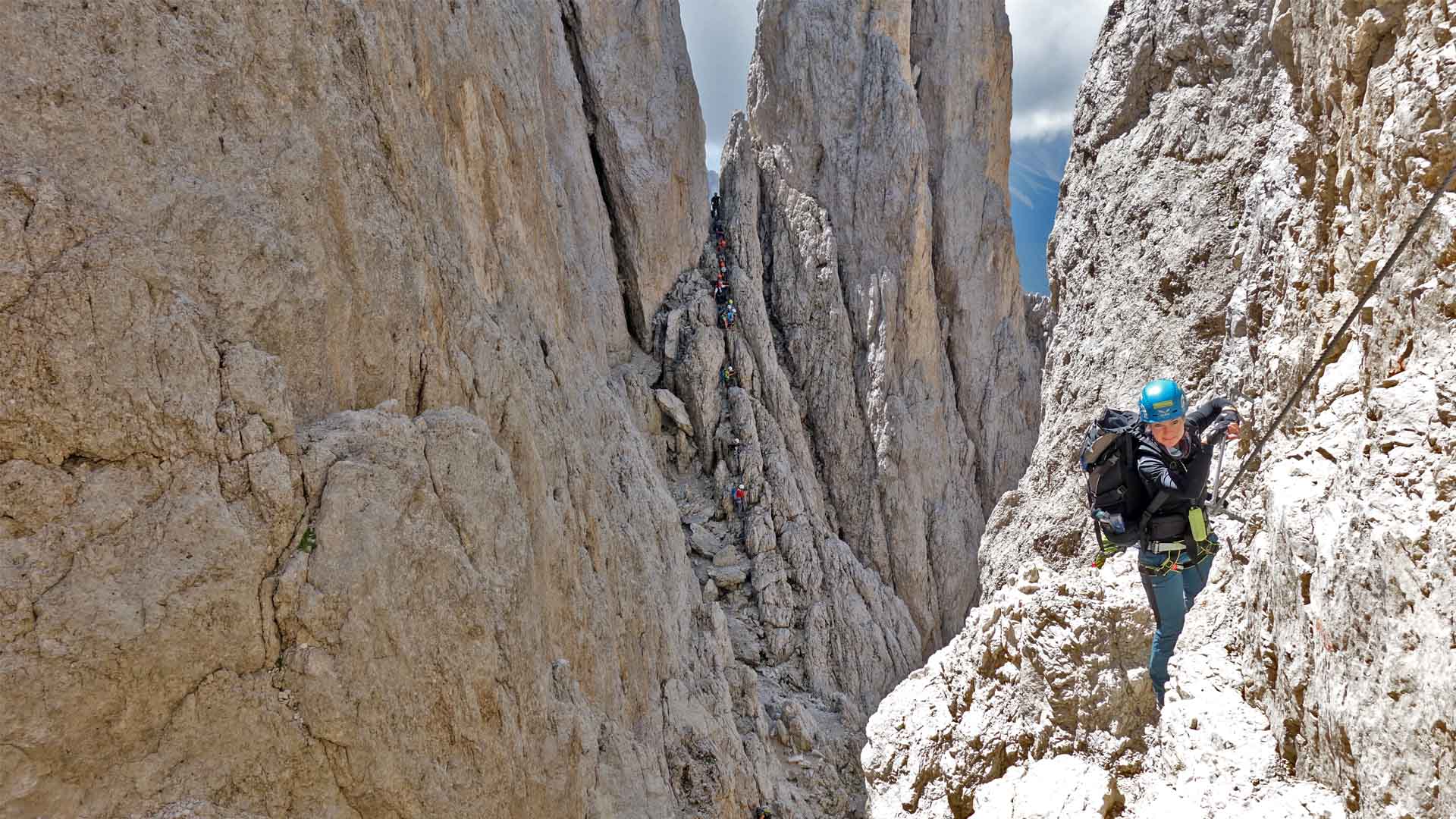Klettersteiggehergruppe aus mindestens 15 Personen steigt in Reihe einen schmalen Felsrücken am Rosengarten auf.