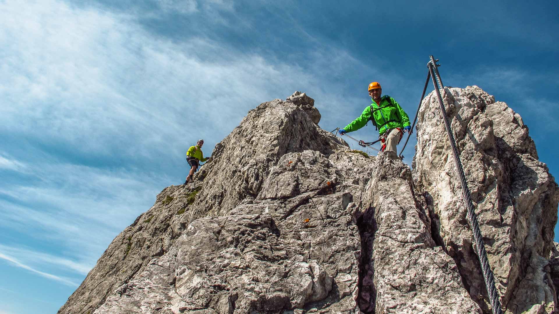 Zwei Klettersteiggeher am Drahtseil eines Felsgrats in den Hohen Tauern, Klettersteigset und Karabiner sichtbar.