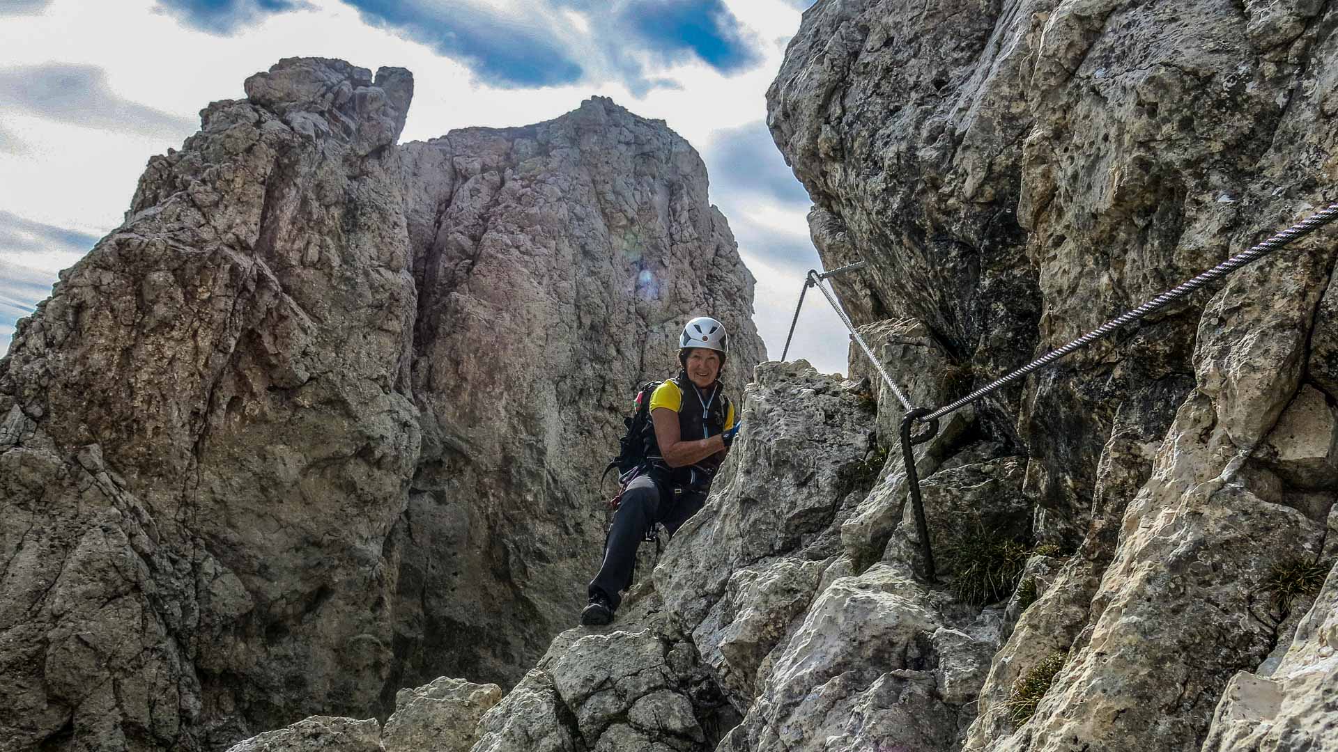 Klettersteiggeher klettert am Drahtseil zwischen Kalkfelsnadeln am Sella Pass in den Dolomiten bei wechselhaftem Wetter.