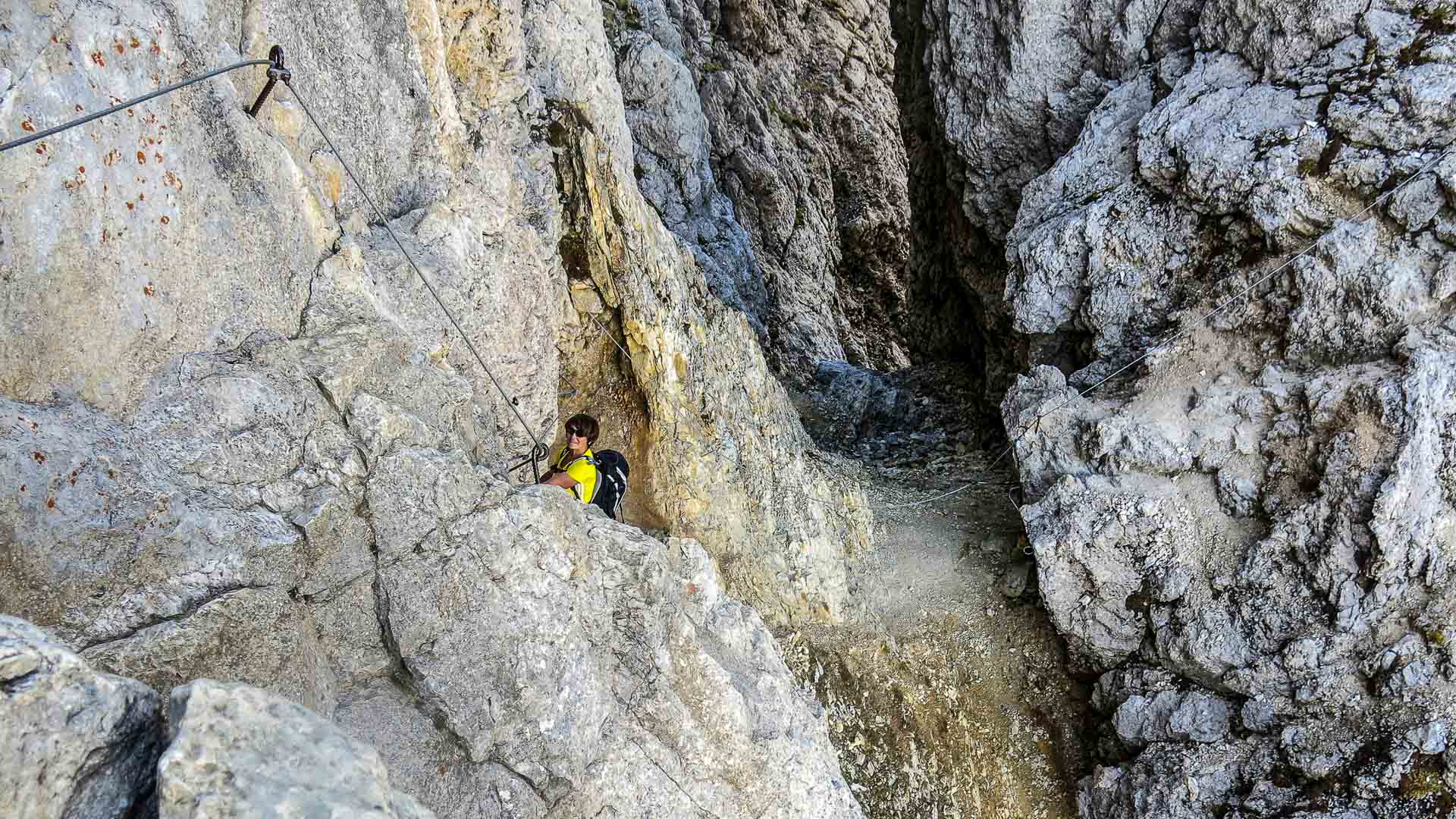 Klettersteiggeher hält sich in einer engen Kalksteinspalte am Stahlseil fest, Klettersteig am Sella Pass in den Dolomiten.
