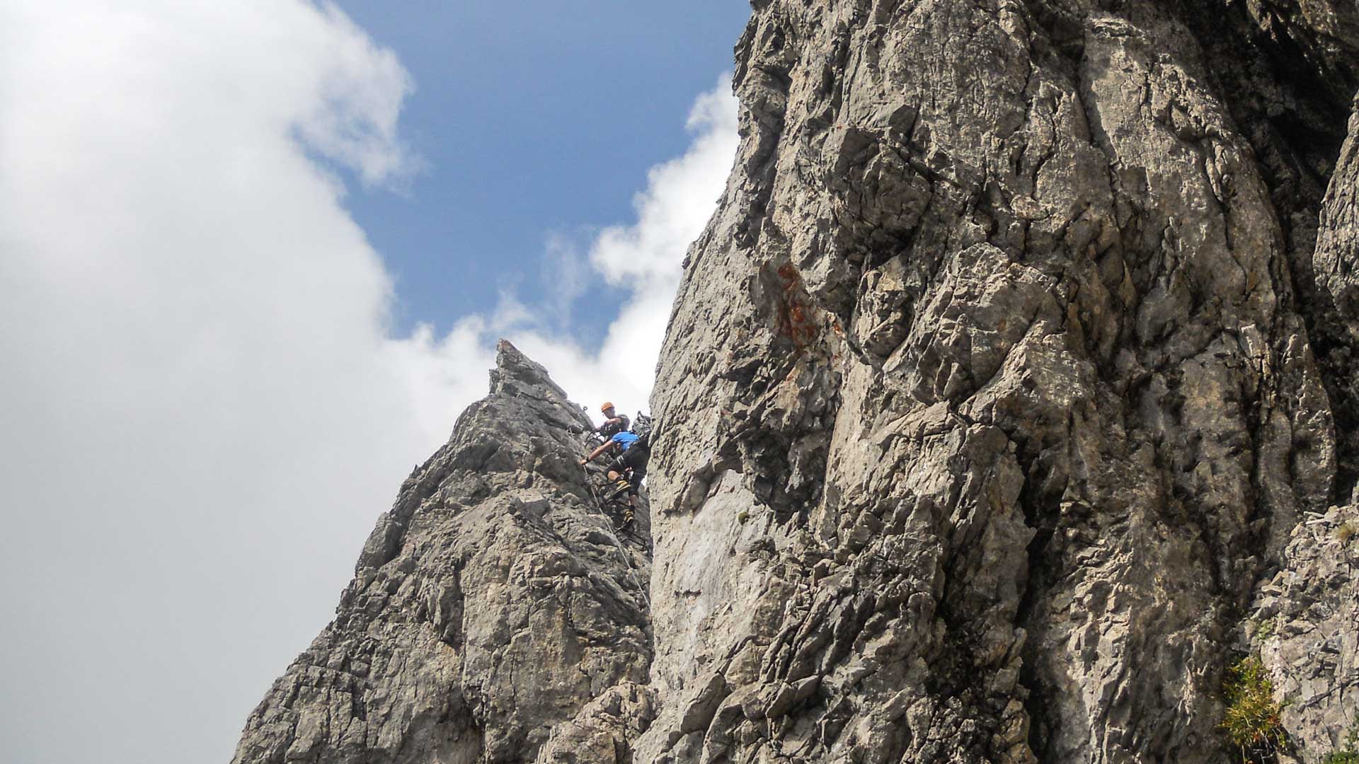 Zwei Klettersteiggeher im Aufstieg an einem gezackten Kalkfelsgrat bei einem Klettersteig im Allgäu.