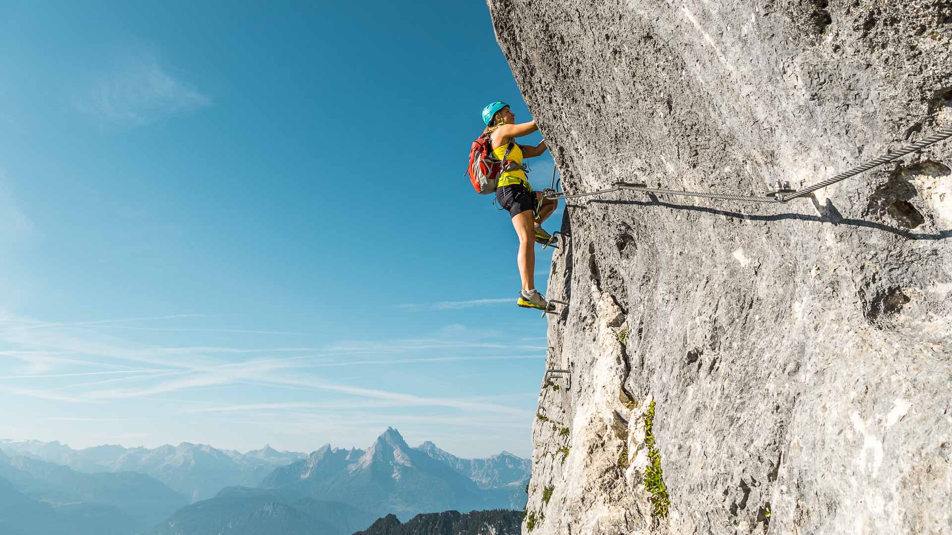 Klettersteiggeher mit Helm und Rucksack klettert am Fixseil des Fotoquergangs am Untersberg auf Tritteisen aufwärts.