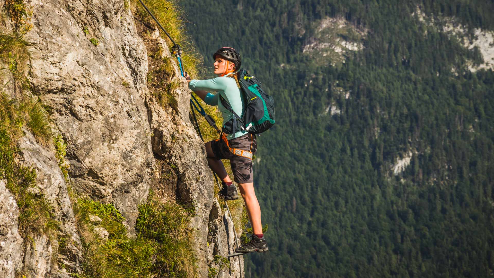 Frau mit Helm und Klettersteig-Set klettert an senkrechter Kalkfelswand am Grünstein in den Berchtesgadener Alpen.