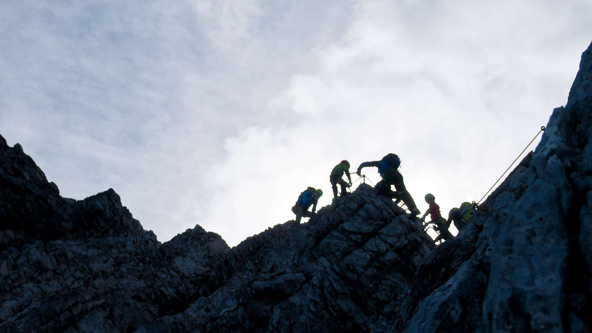Fünf Klettersteiggeher steigen am Felsgrat der Alpspitze auf, gesichert an einem Stahlseil.