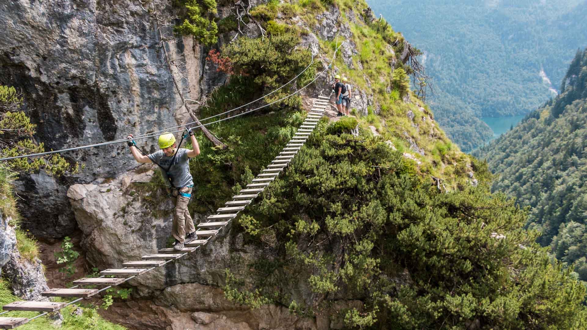 Klettersteiggeher überquert eine Hängeleiter aus Holzbrettern und Stahlseilen am Grünstein bei Berchtesgaden.