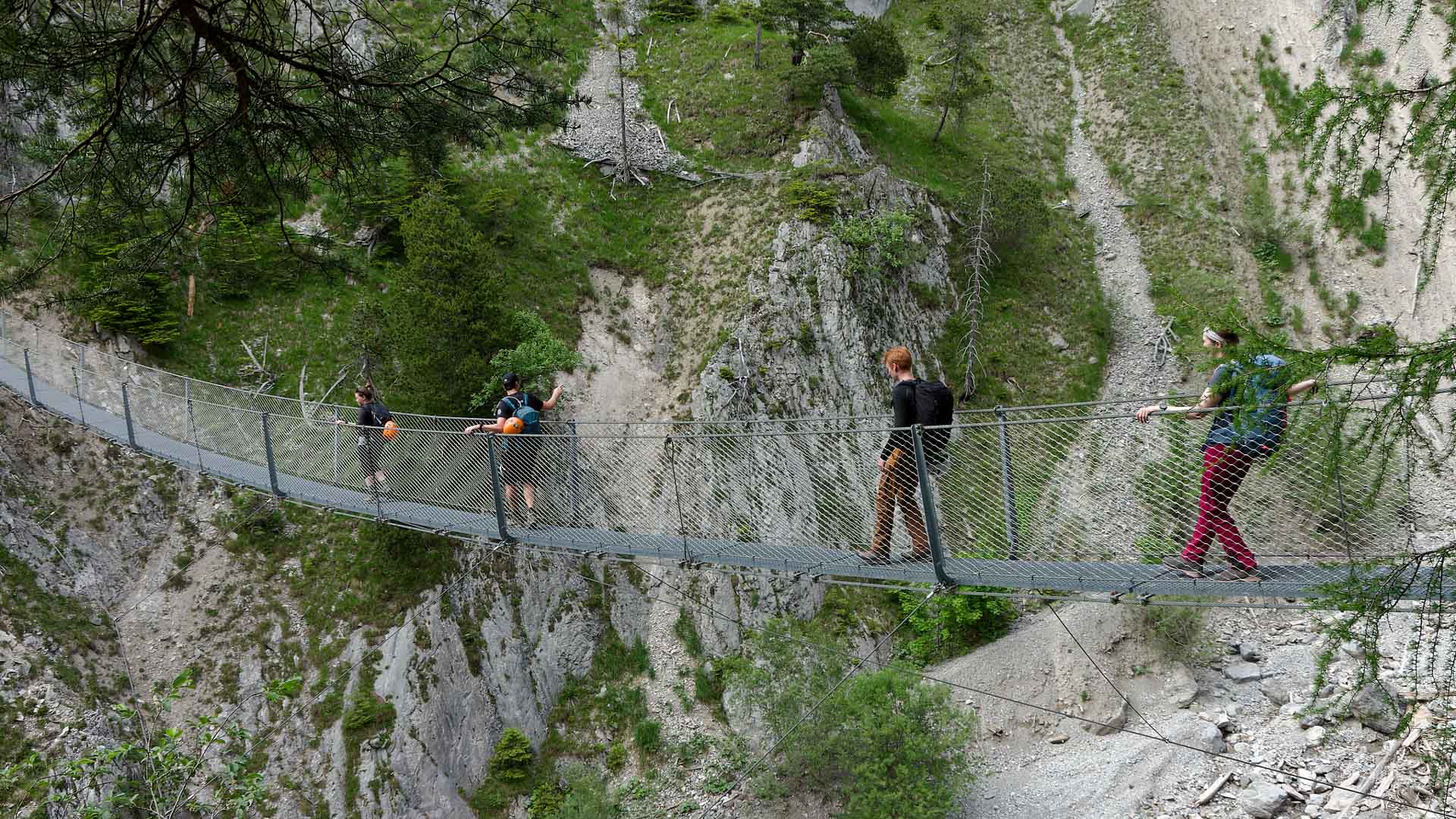 Vier Wanderer überqueren die Hängebrücke aus Stahlseil am Mittenwalder Höhenweg über steilem Kalkfels.