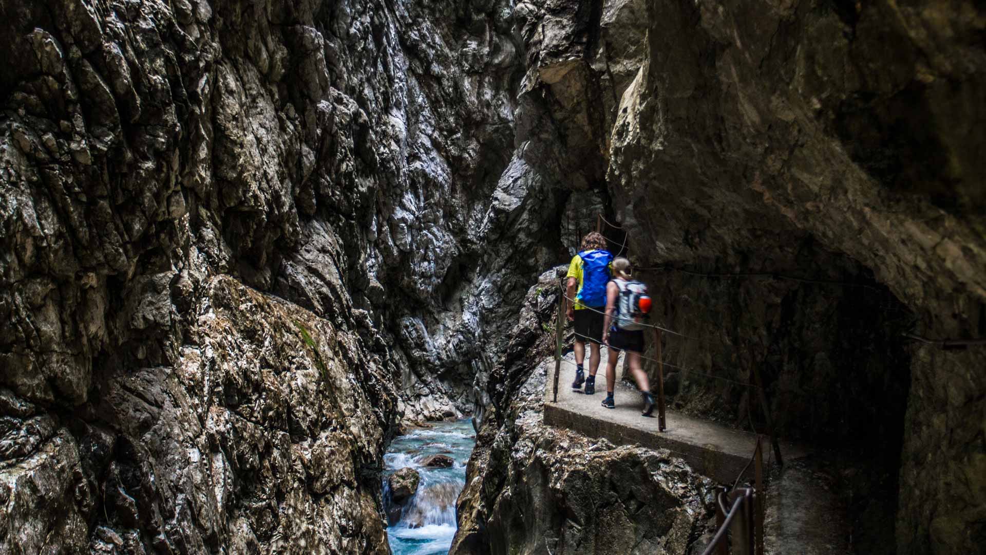 Klettersteig Höllentalklamm Zugspitze: zwei Personen mit Rucksäcken auf gesichertem Felsweg über türkisem Wildbach