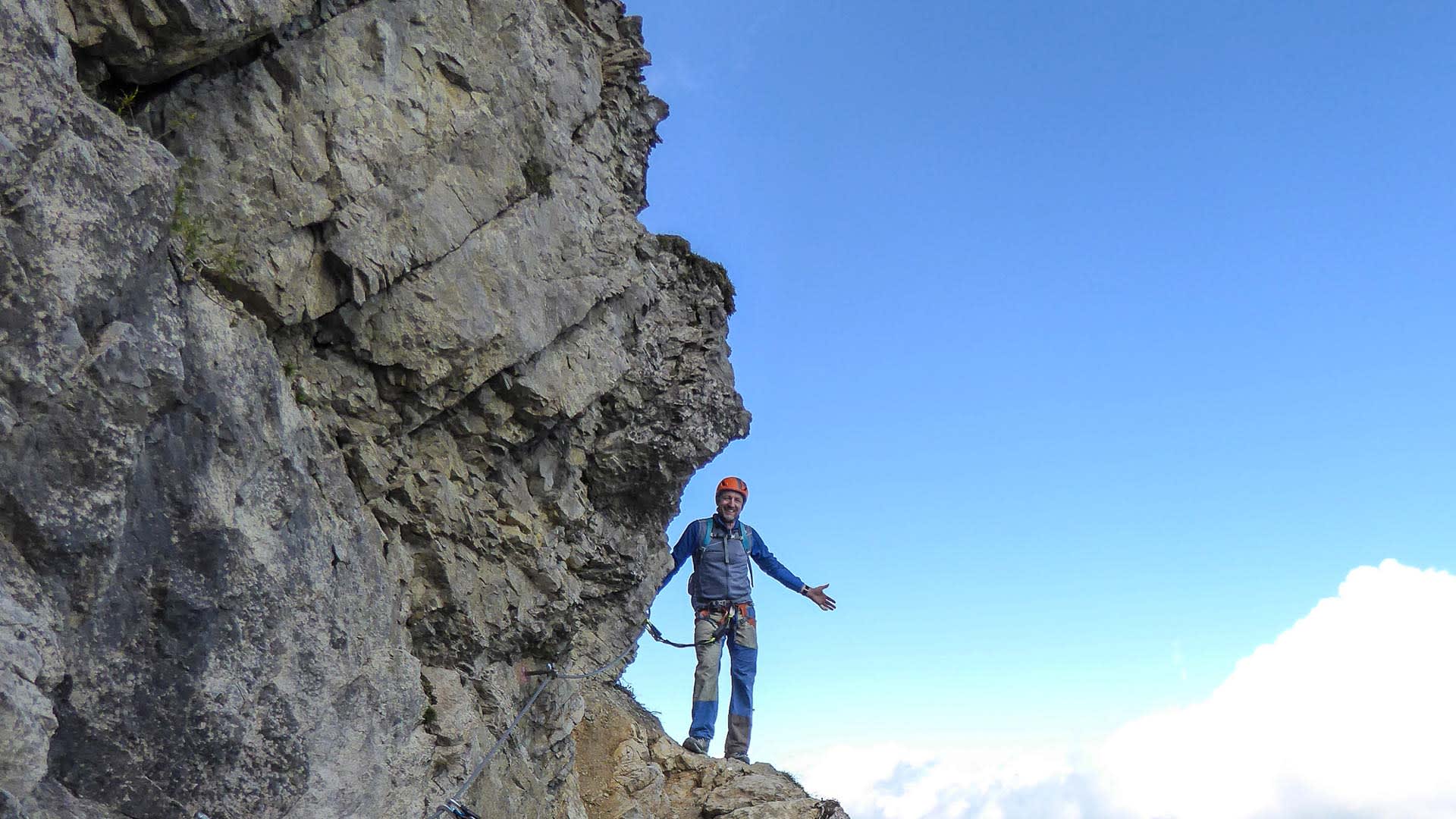 Klettersteiggeher mit Helm und Klettersteigset steht an senkrechter Kalkfelswand des Salewa Klettersteigs Oberjoch.