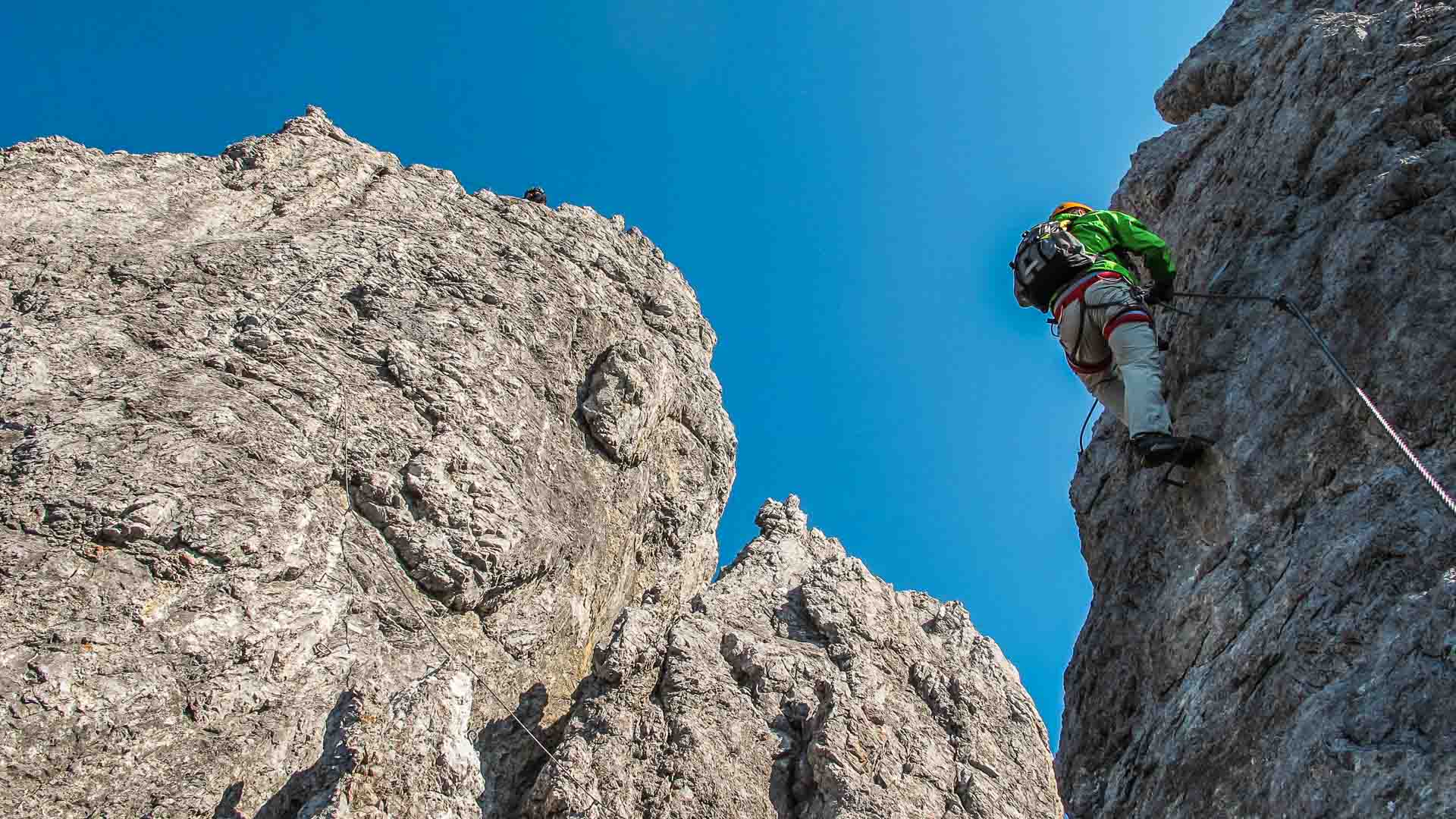 Klettersteig Königsjodler in den Berchtesgadener Alpen: Kletterer mit grüner Jacke und orangem Helm steigt senkrechte Kalkwand
