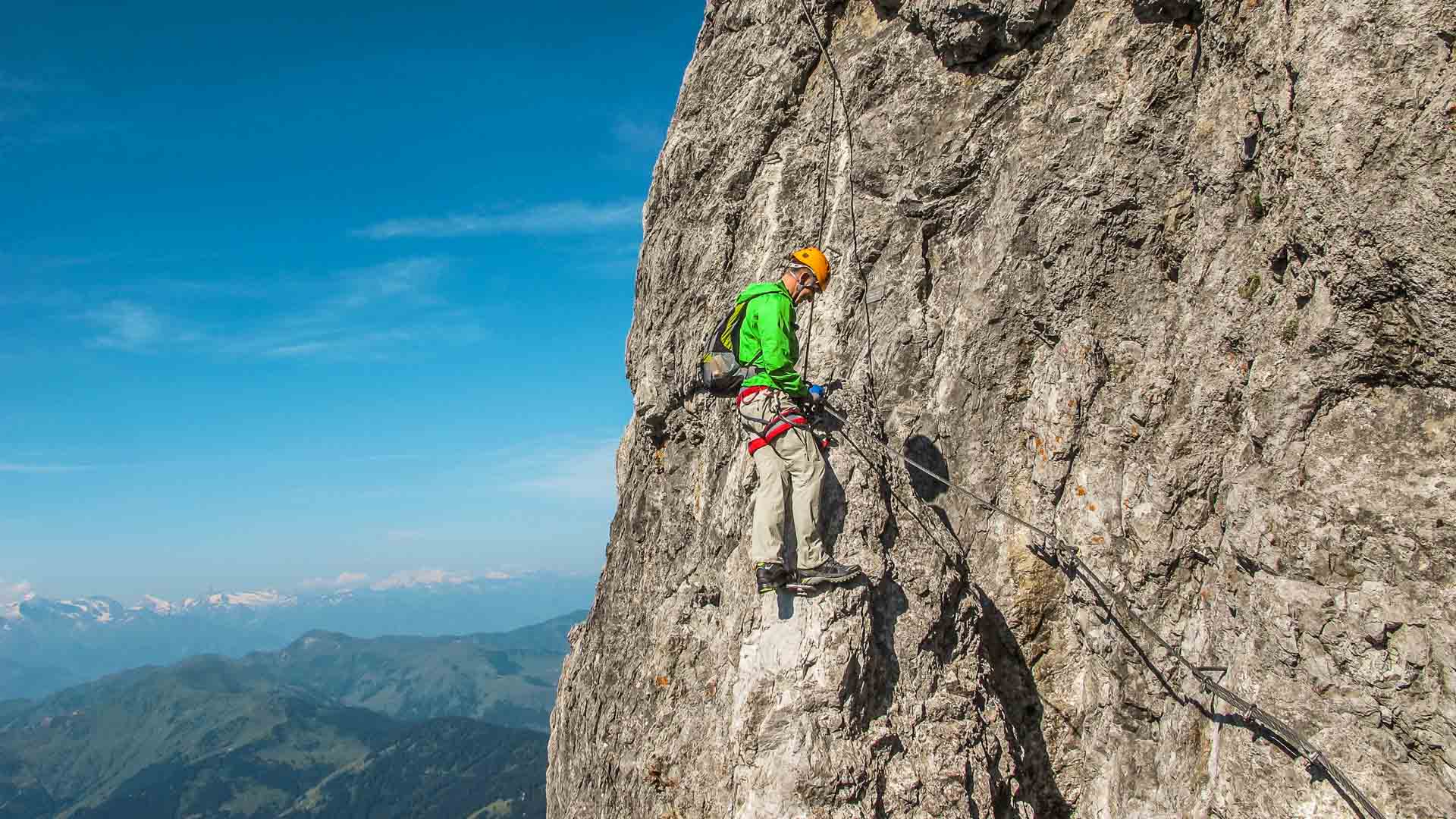 Person mit Helm und Gurt gesichert an steiler Kalkfelswand beim Klettersteig Königsjodler in den Berchtesgadener Alpen.