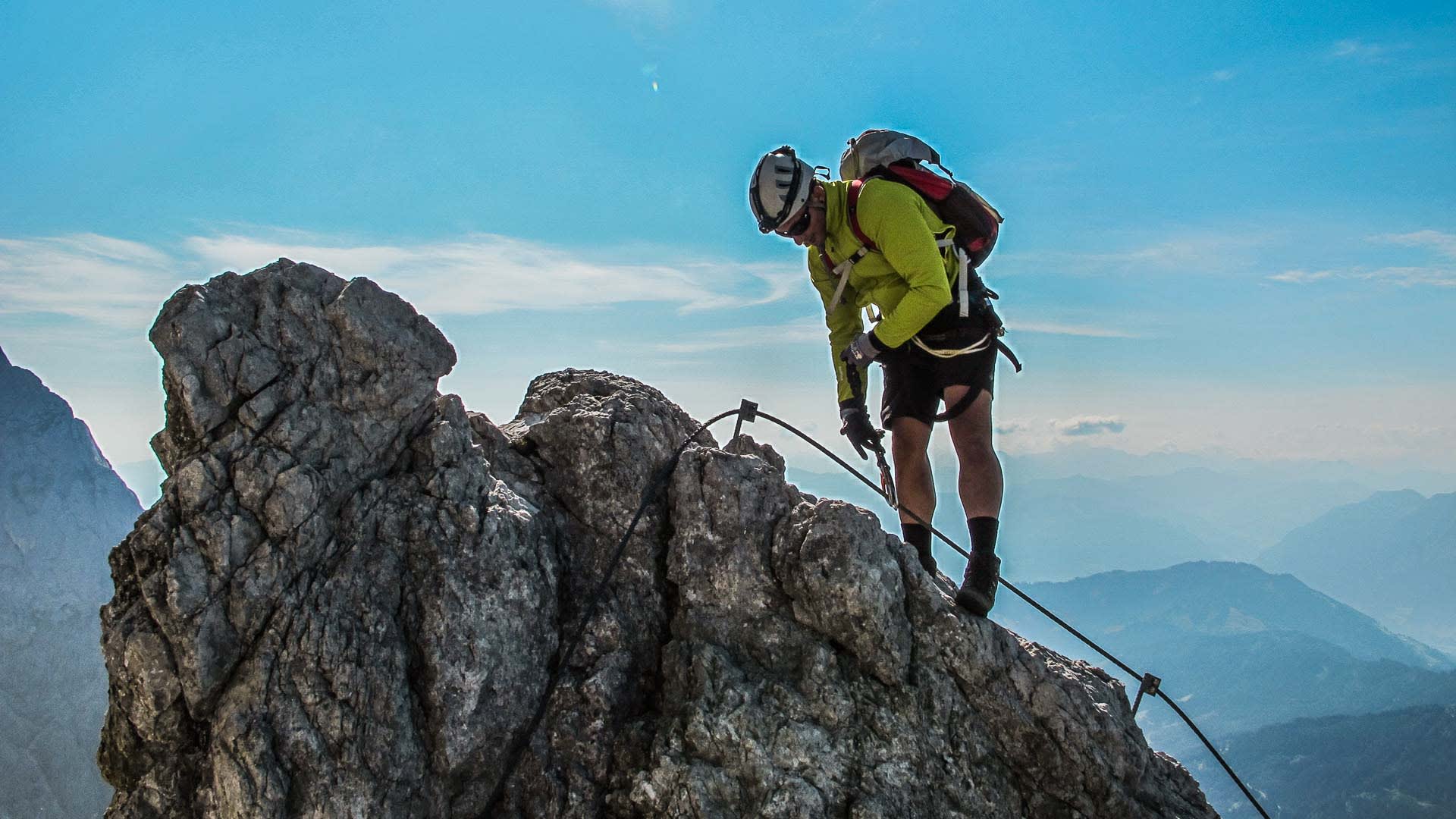 Person am Fixseil auf dem Felsengrat des Königsjodler-Klettersteigs in den Berchtesgadener Alpen mit Blick ins weite Tal.