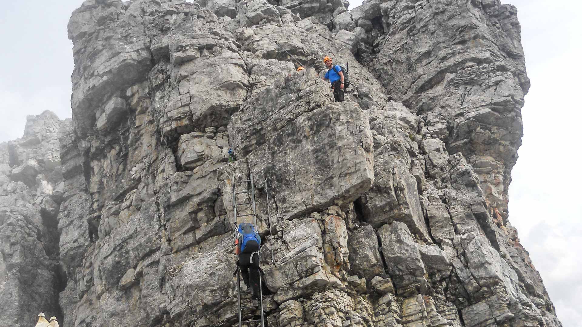 Klettersteiggeher steigen an Metallsprossen-Leitern und Drahtseil einer Kalkfelswand im Mindelheimer Klettersteig auf.