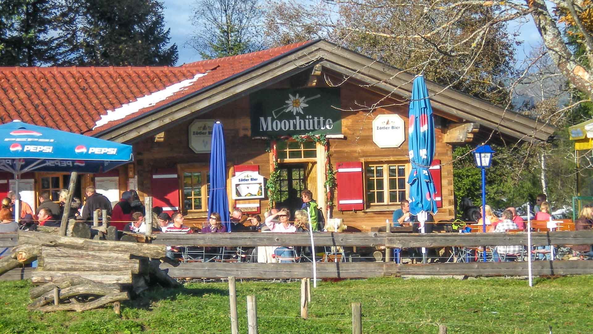 Moorhütte im Allgäu mit Außenterrasse und Klettersteiggehern auf Holzbänken als Rastpunkt am Iseler.