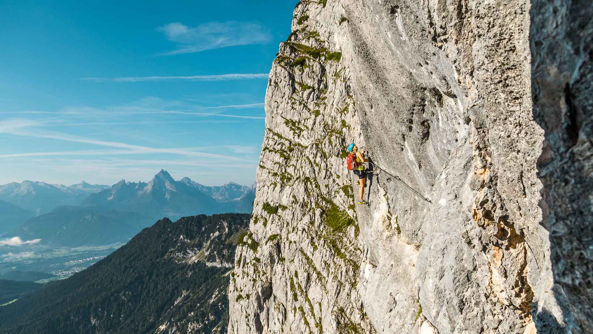 Ein Klettersteiggeher traversiert einen Quergang am Untersberg, im Hintergrund der Watzmann und das Tal.
