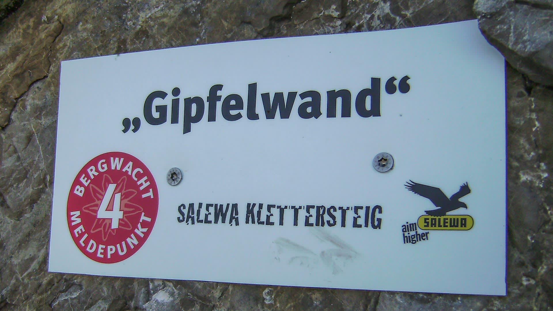 Hinweisschild Gipfelwand am Salewa Klettersteig Iseler mit Bergwacht-Meldepunkt und Salewa-Logo an grauem Fels.