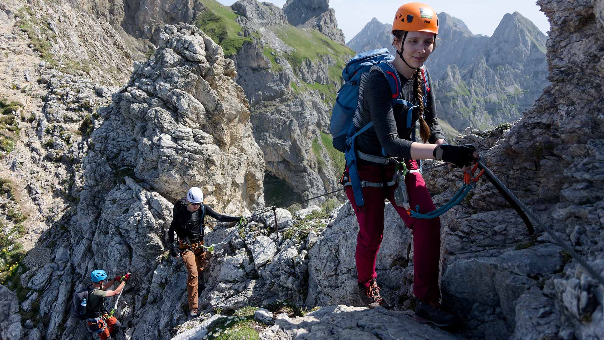 Drei Klettersteiggeher mit Helm, Gurt und Klettersteigset steigen am Stahlseil des Mittenwalder Höhenwegs im Karwendel auf.