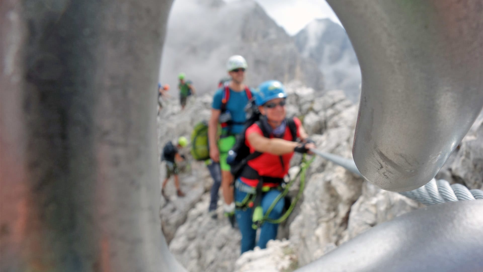 Vier Klettersteiggeher steigen am Rosengarten über zerklüfteten Kalkfels, gesichert am Stahlseil der Via Ferrata.