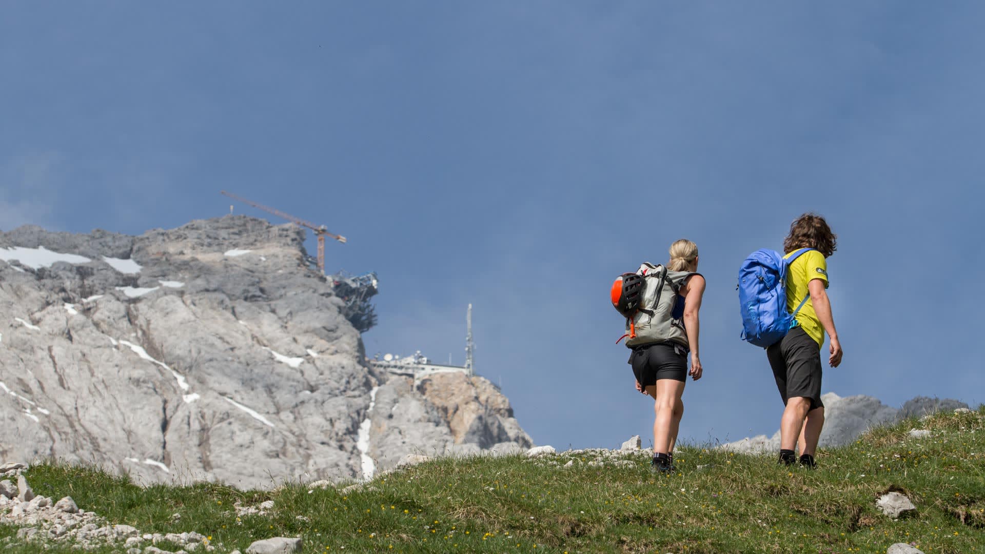 Klettersteig Zugspitze: Zwei Personen steigen über einen Grashang im Höllental auf, im Hintergrund der Zugspitzgipfel