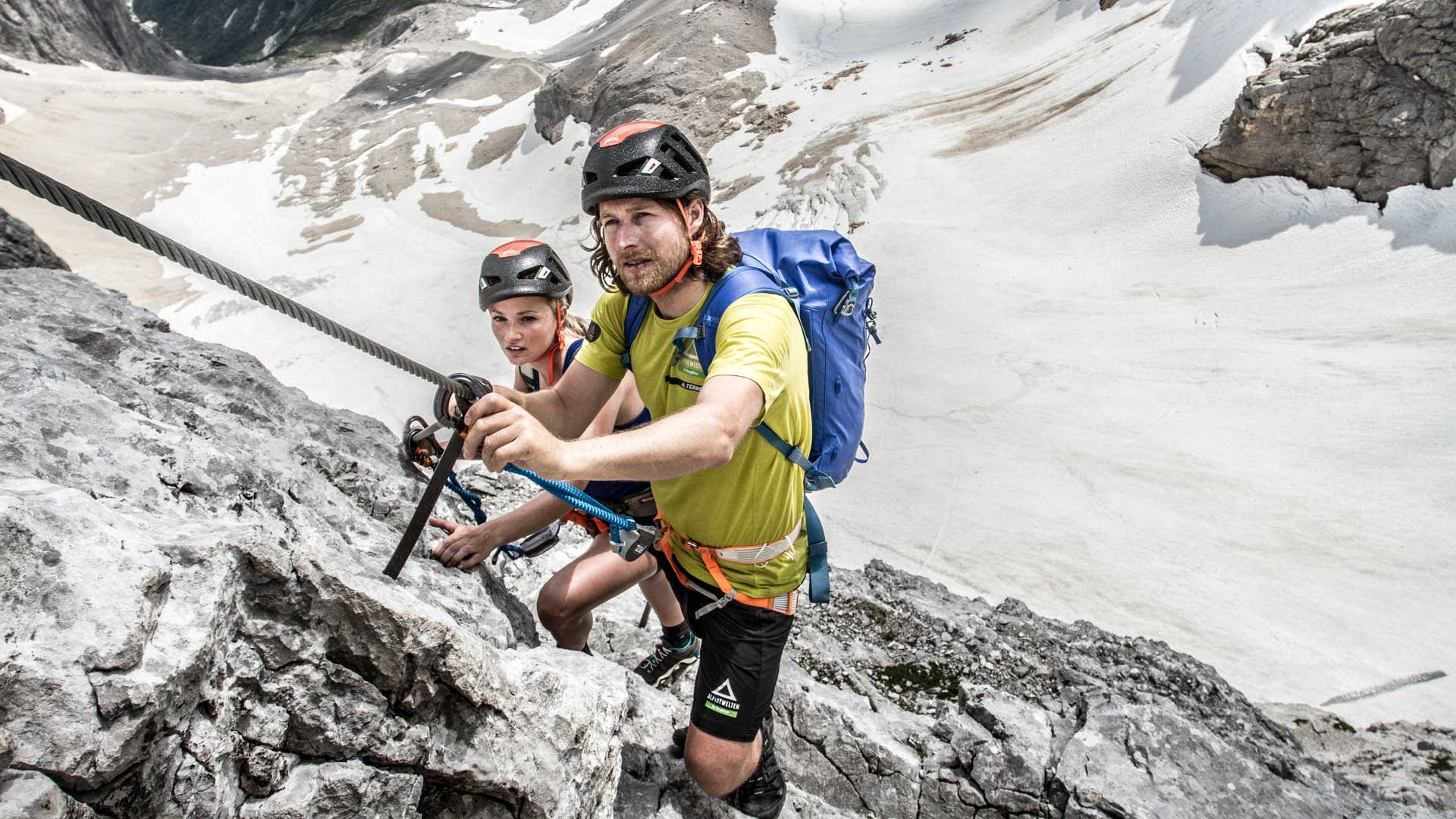 Zwei Personen mit Helm und Klettergurt greifen das Fixseil beim Zugspitze Klettersteig im Höllental, im Hintergrund