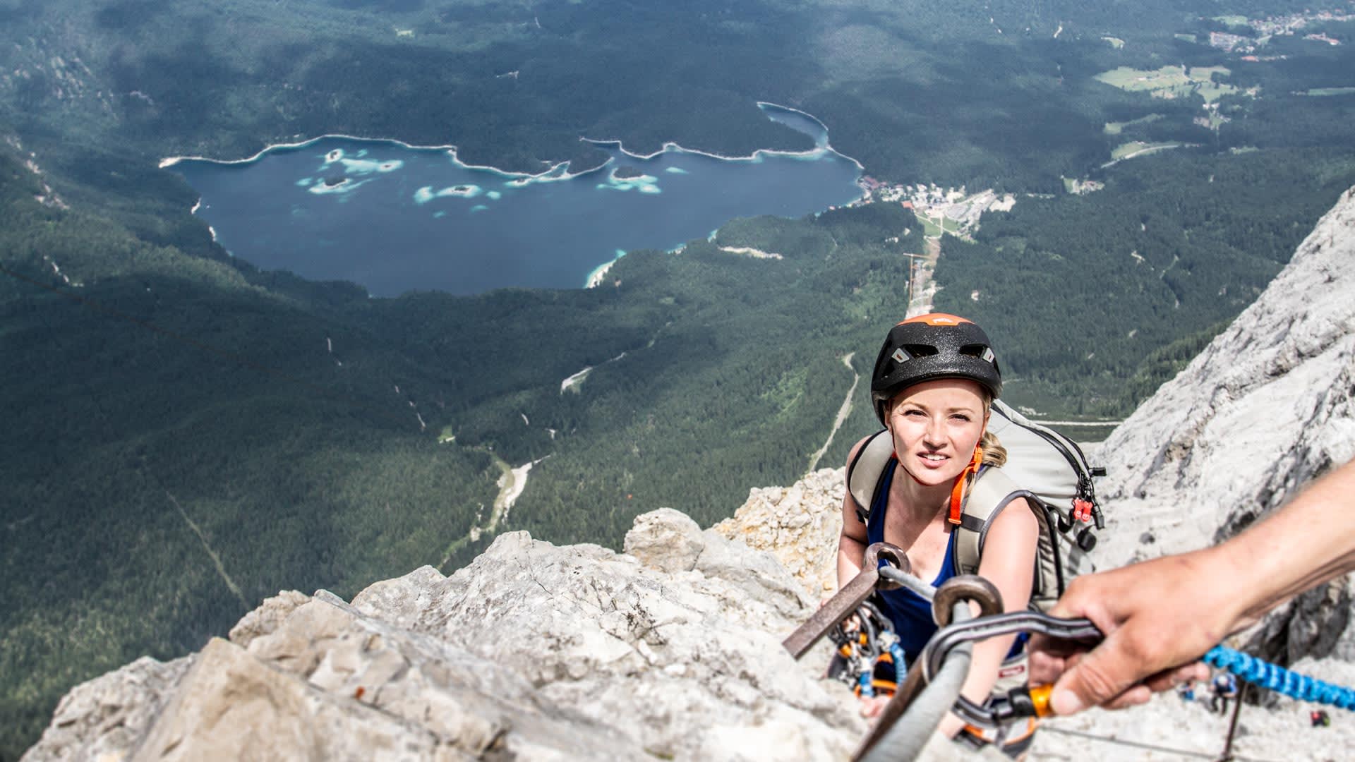 Klettersteig Zugspitze: Klettersteiggeherin mit Helm, Gurt und Karabiner an Eisenbügeln aus Kalkfels