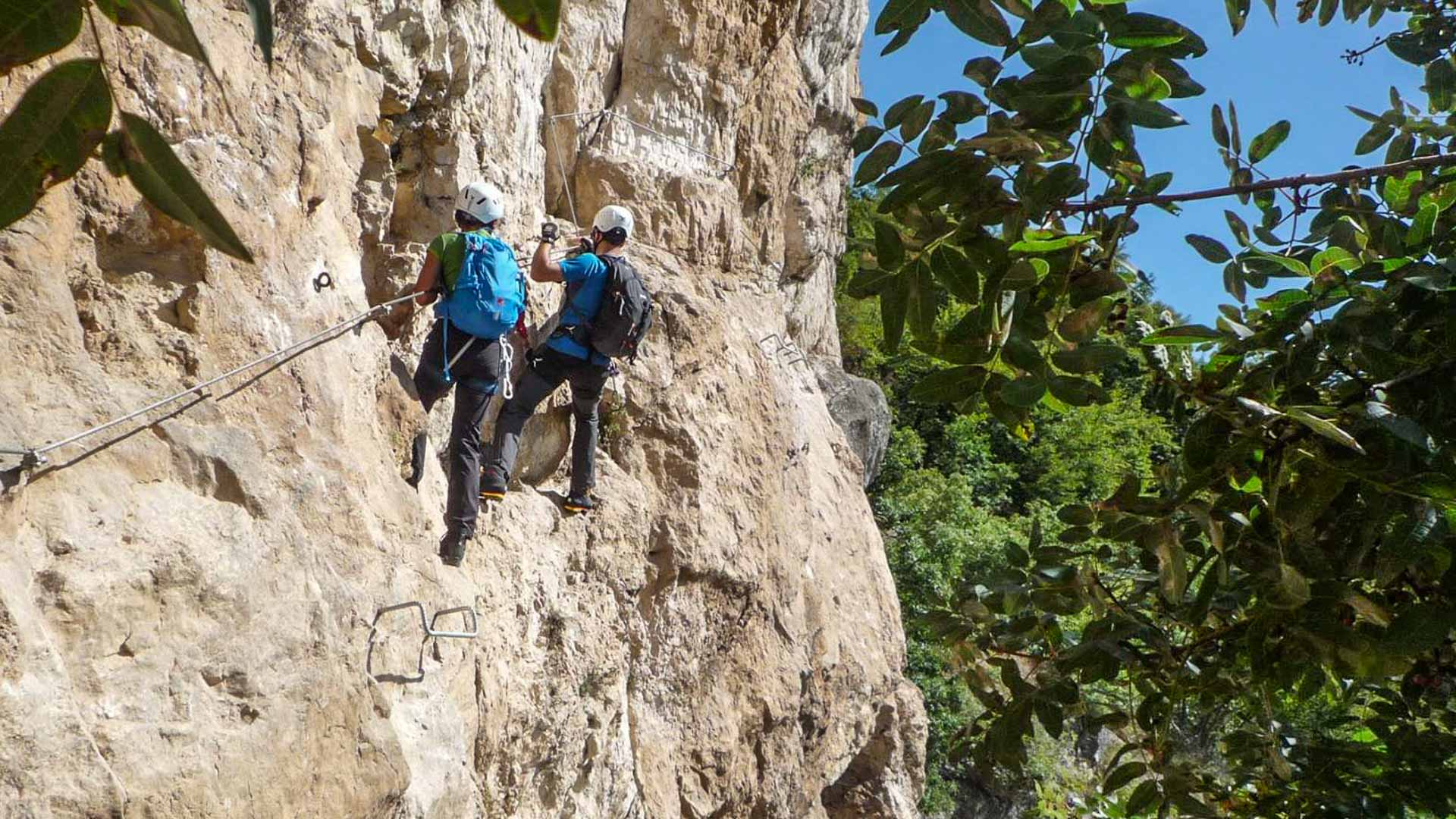 Zwei Klettersteiggeher steigen an senkrechter Kalkfelswand mit Eisenbügeln und Drahtseil am Gardasee auf.