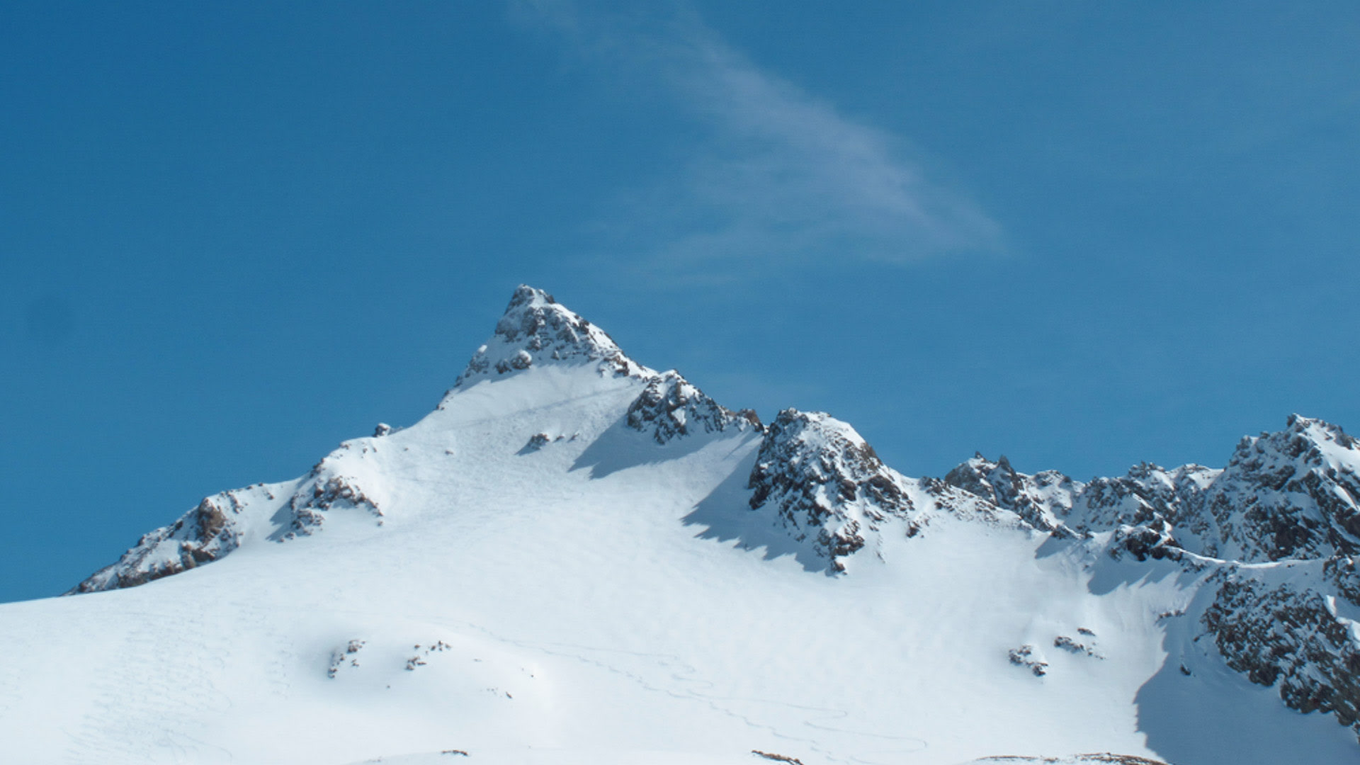 Schneeschuhtour zur Dreiländerspitze: verschneiter Gipfel mit Felsgrat und Hochplateau unter blauem Himmel.