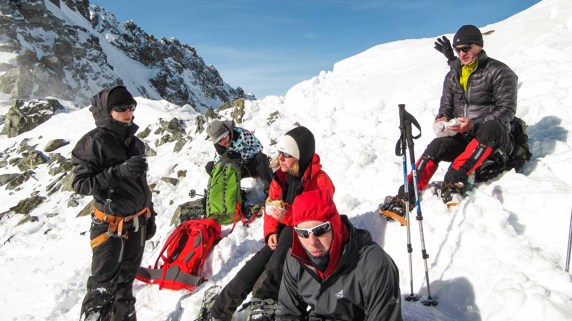 Fünf Personen pausieren auf einer Schneeschuhtour in der Silvretta auf felsig-schneebedecktem Untergrund