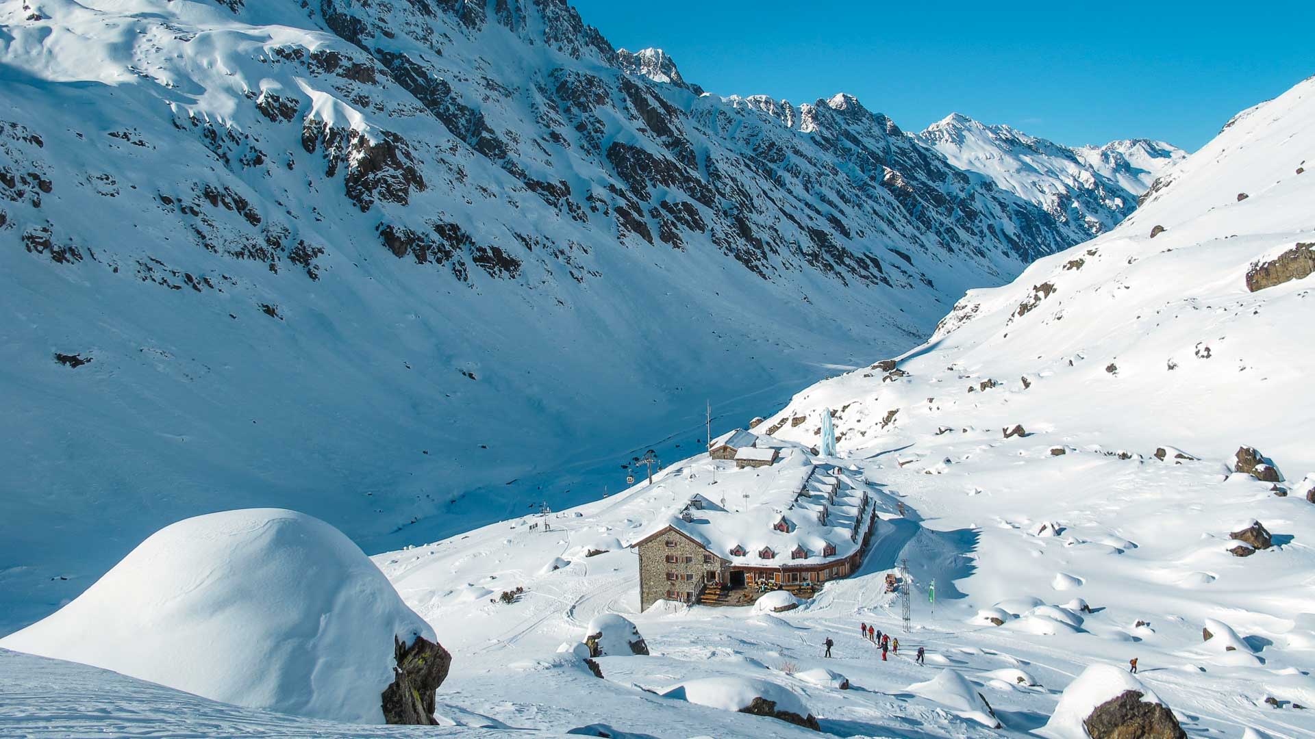 Schneeschuhtour zur Jamtalhütte: Natursteingebäude mit rotem Fensterladen im verschneiten Hochtal der Silvretta.