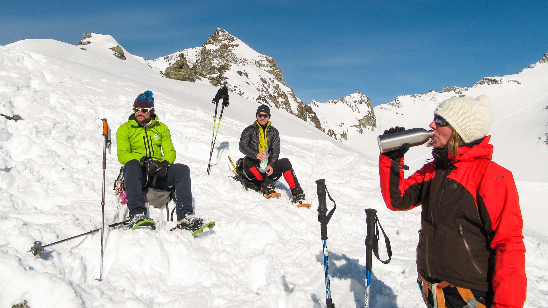 Drei Schneeschuhwanderer pausieren auf einem verschneiten Hang der Silvretta vor felsigem Gipfelpanorama.