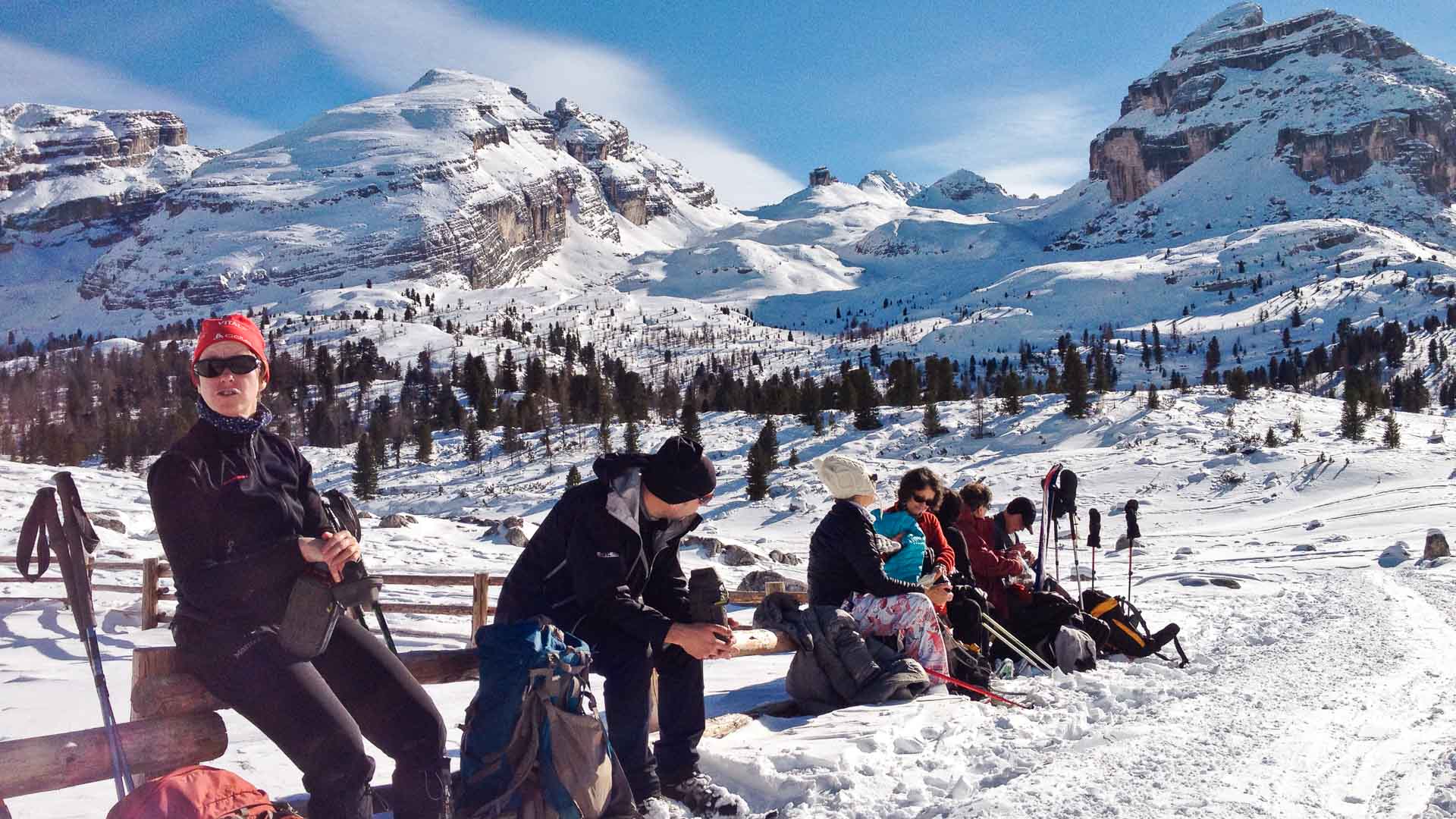 Gruppe pausiert bei der Schneeschuhtour an einem Holzzaun auf dem verschneiten Hochplateau der Fanes mit Felsgipfeln der Dolomiten