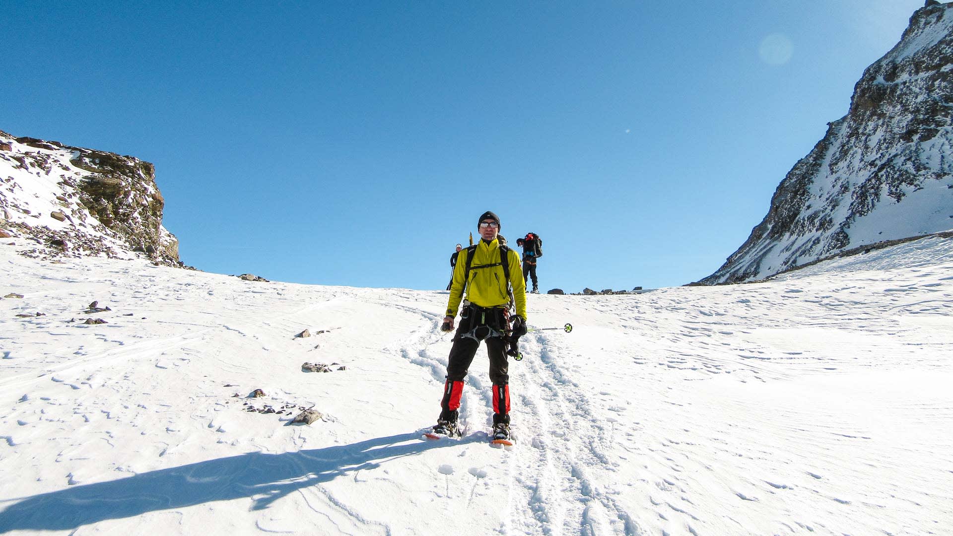 Zwei Schneeschuhwanderer steigen einen verschneiten Felshang am Piz Buin in der Silvretta auf.