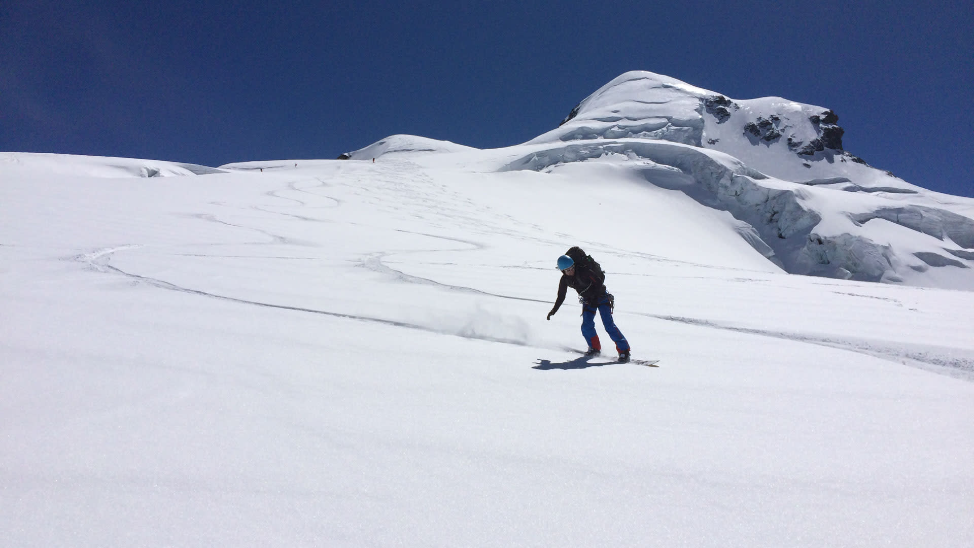 Person fährt bei der Skitour am Gletscherhang des Piz Buin mit Splitboard talwärts, im Hintergrund Seracs und blauer Himmel.