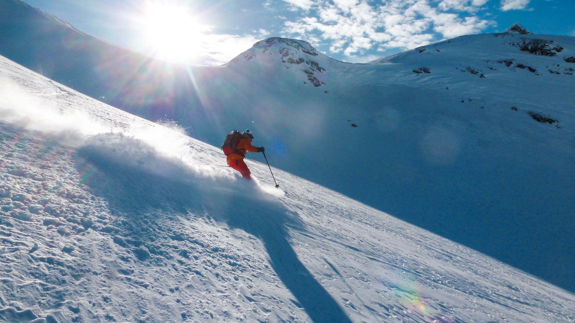 Skitourengeher in oranger Jacke fährt auf einem Steilhang bei der Heidelberger Hütte Ischgl im Pulverschnee ab