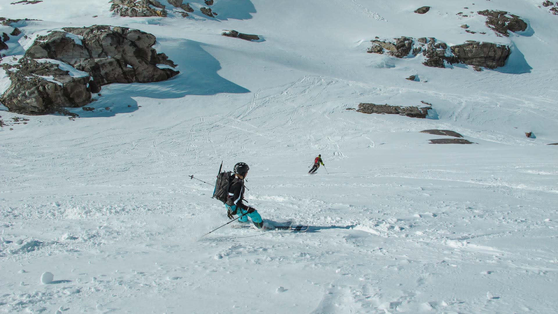 Zwei Skitouren-Abfahrer kurven einen breiten, schneebedeckten Hang am Piz Buin hinunter, Schnee wird aufgewirbelt.