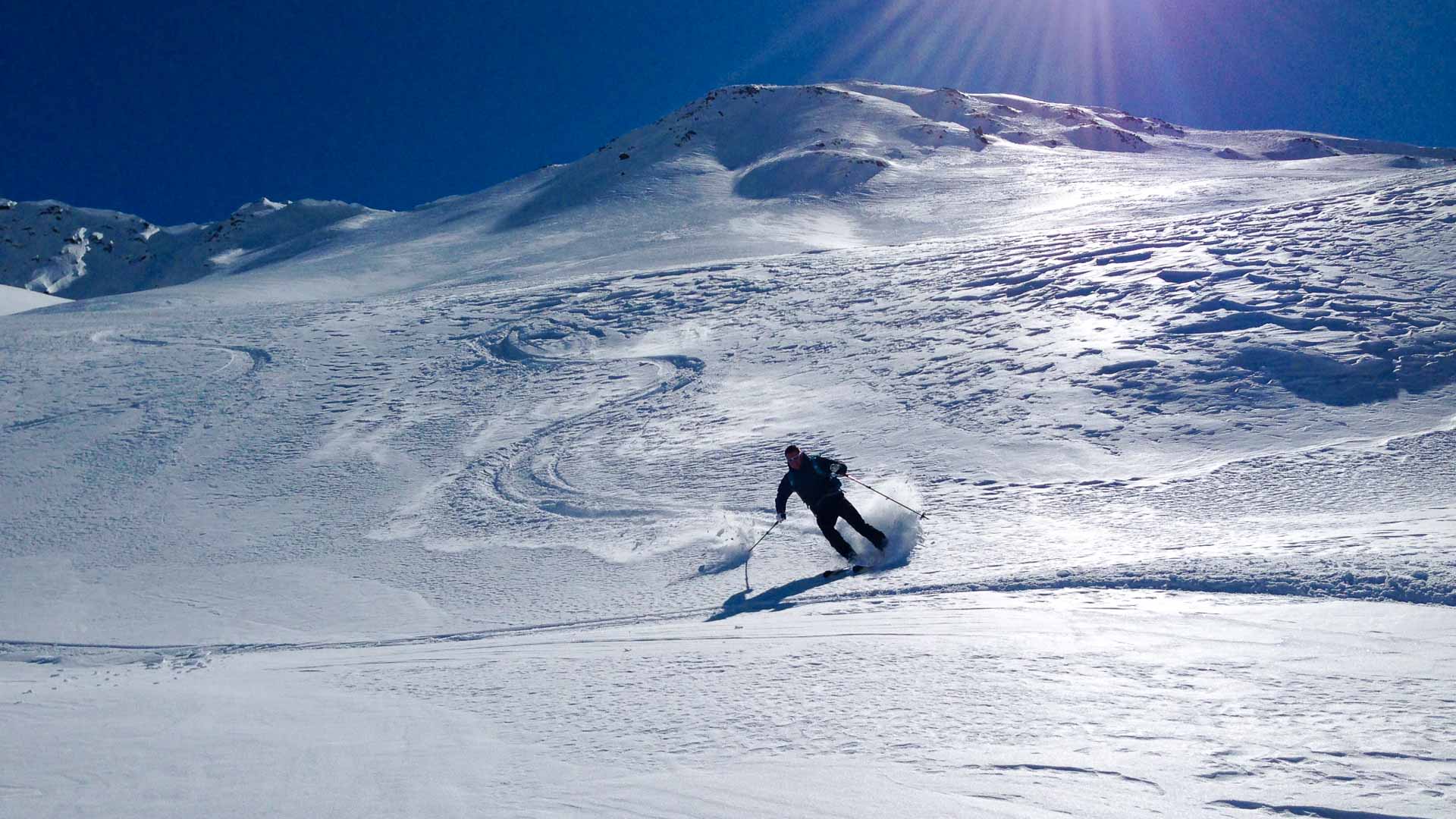 Skitourengeher fährt auf Skiern einen schneebedeckten Hang am Staller Sattel ab, Schwungspuren im Tiefschnee sichtbar.