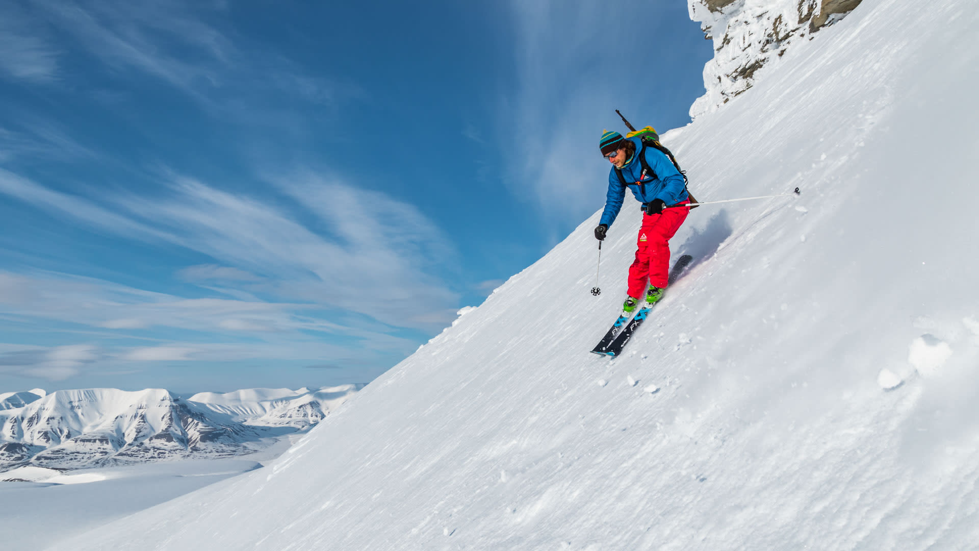 Ein Skitourengeher fährt auf Freeride-Skiern einen steilen Schneehang auf Spitzbergen ab, Froschperspektive.