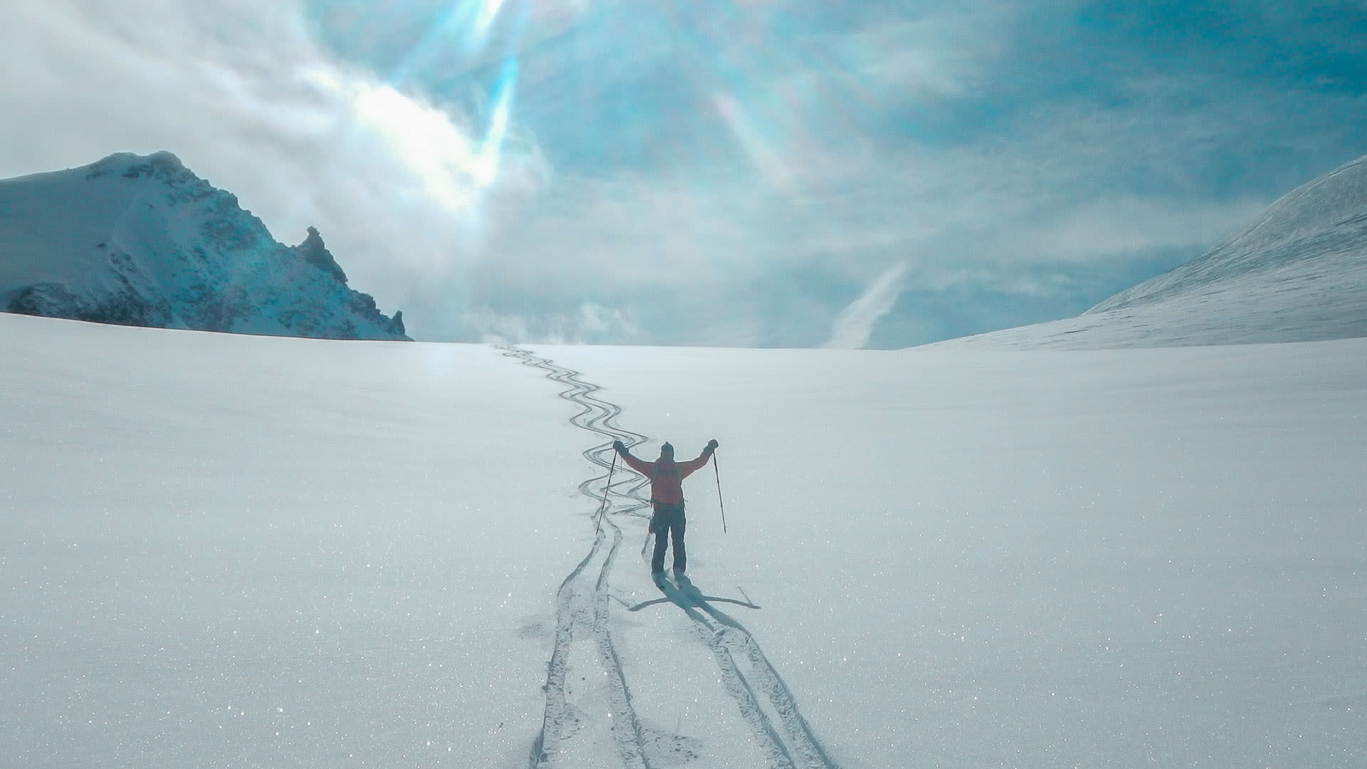 Skitourengeher mit ausgebreiteten Armen auf der Abfahrt vom Strahlhorn ins Mattertal, Skispuren im Schnee.