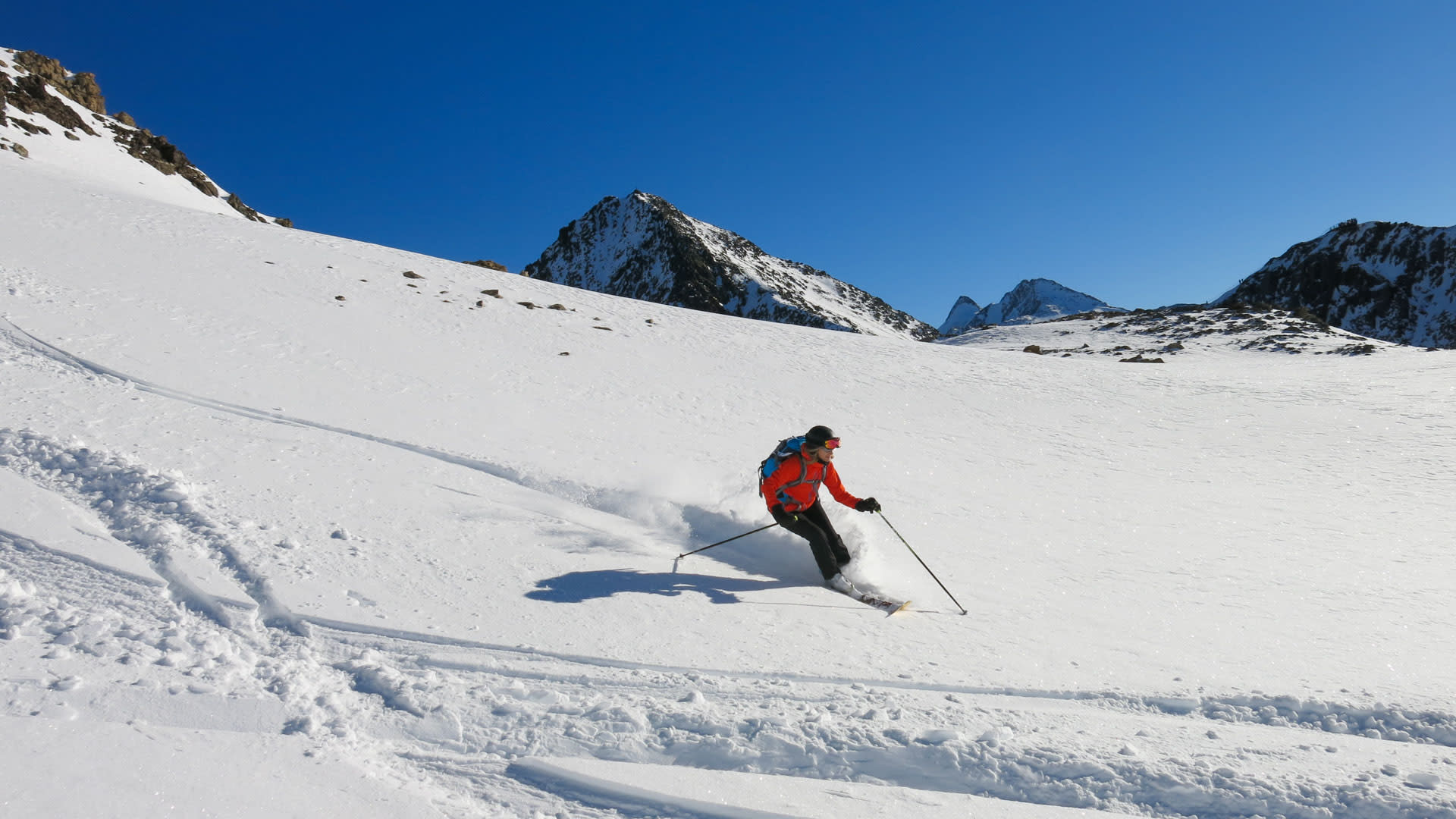 Skitourengeher in roter Jacke fährt mit Pulverschnee-Aufwirbelung einen offenen Hang im Stubai ab.
