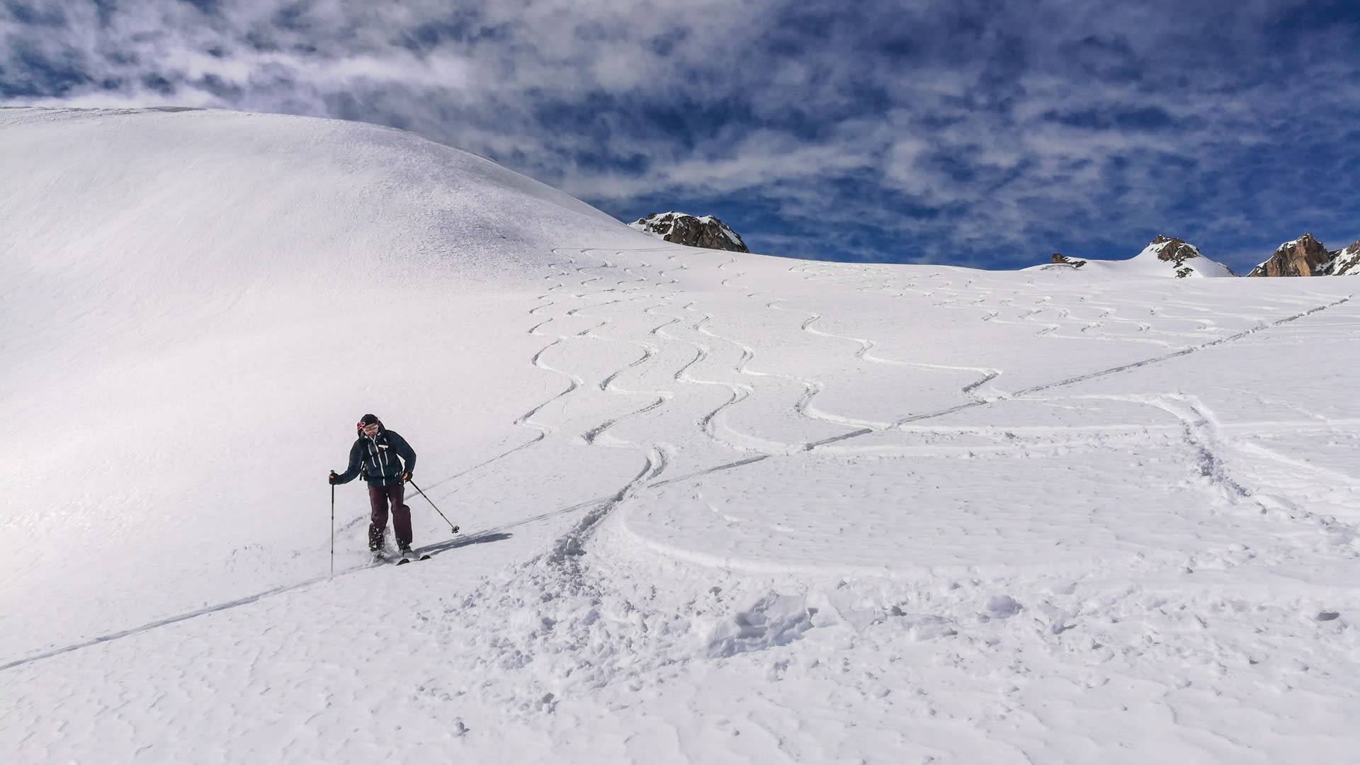 Ein Skitourengeher fährt einen verschneiten Hang im Vinschgau ab, im Schnee sind mehrere Schwünge der Aufstiegsspur sichtbar.