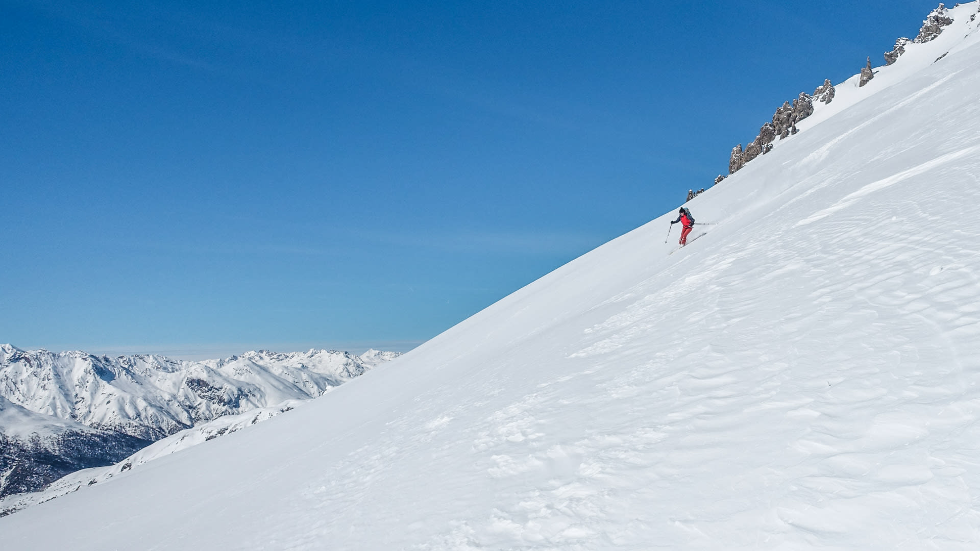 Skitourengeher in roter Jacke fährt einen unberührten Steilhang im Val Müstair auf Skiern ab.