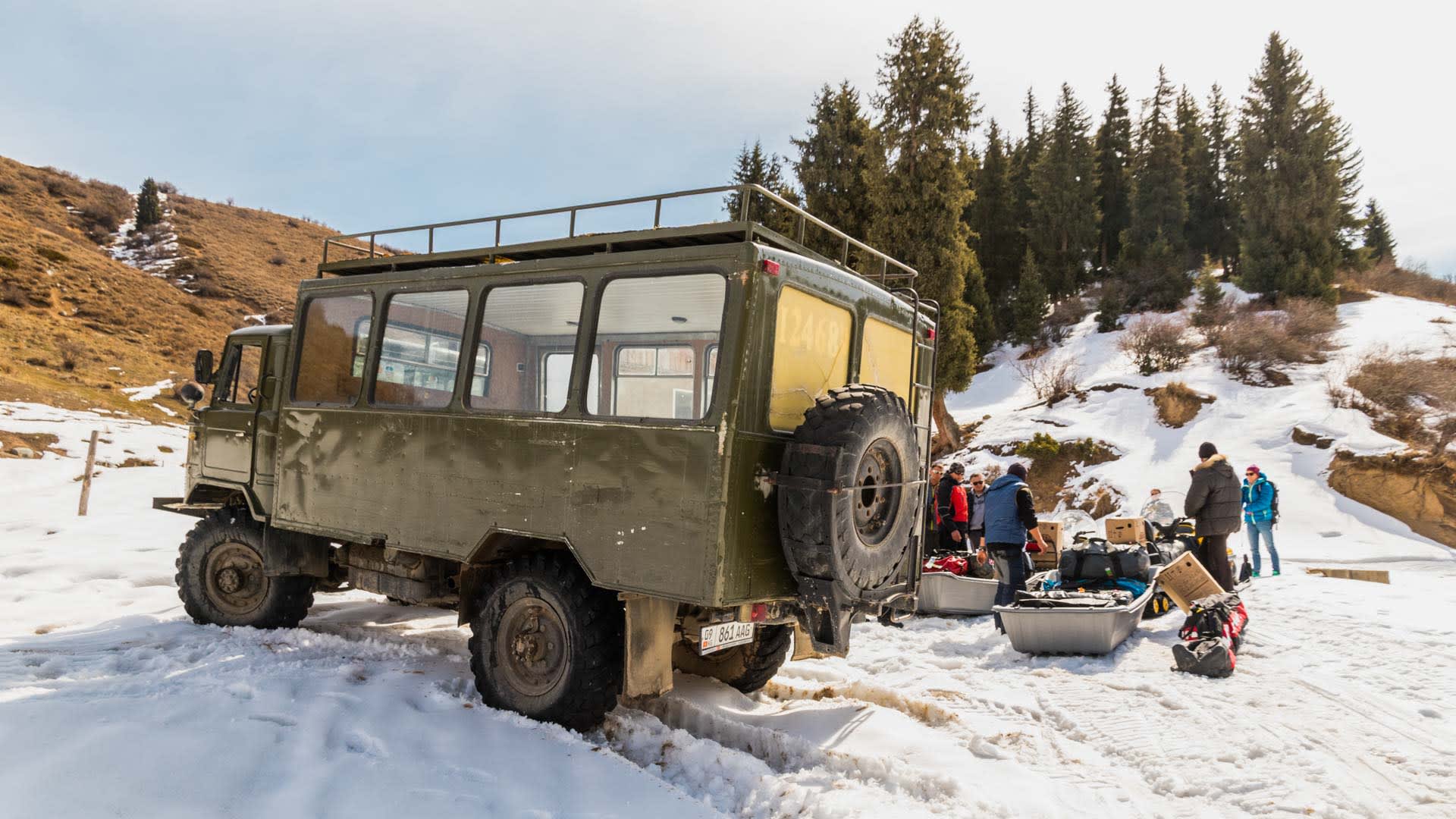 Gruppe von Skitourengehern lädt Gepäck aus einem sowjetischen Geländefahrzeug an der Schneegrenze in Kirgistan.