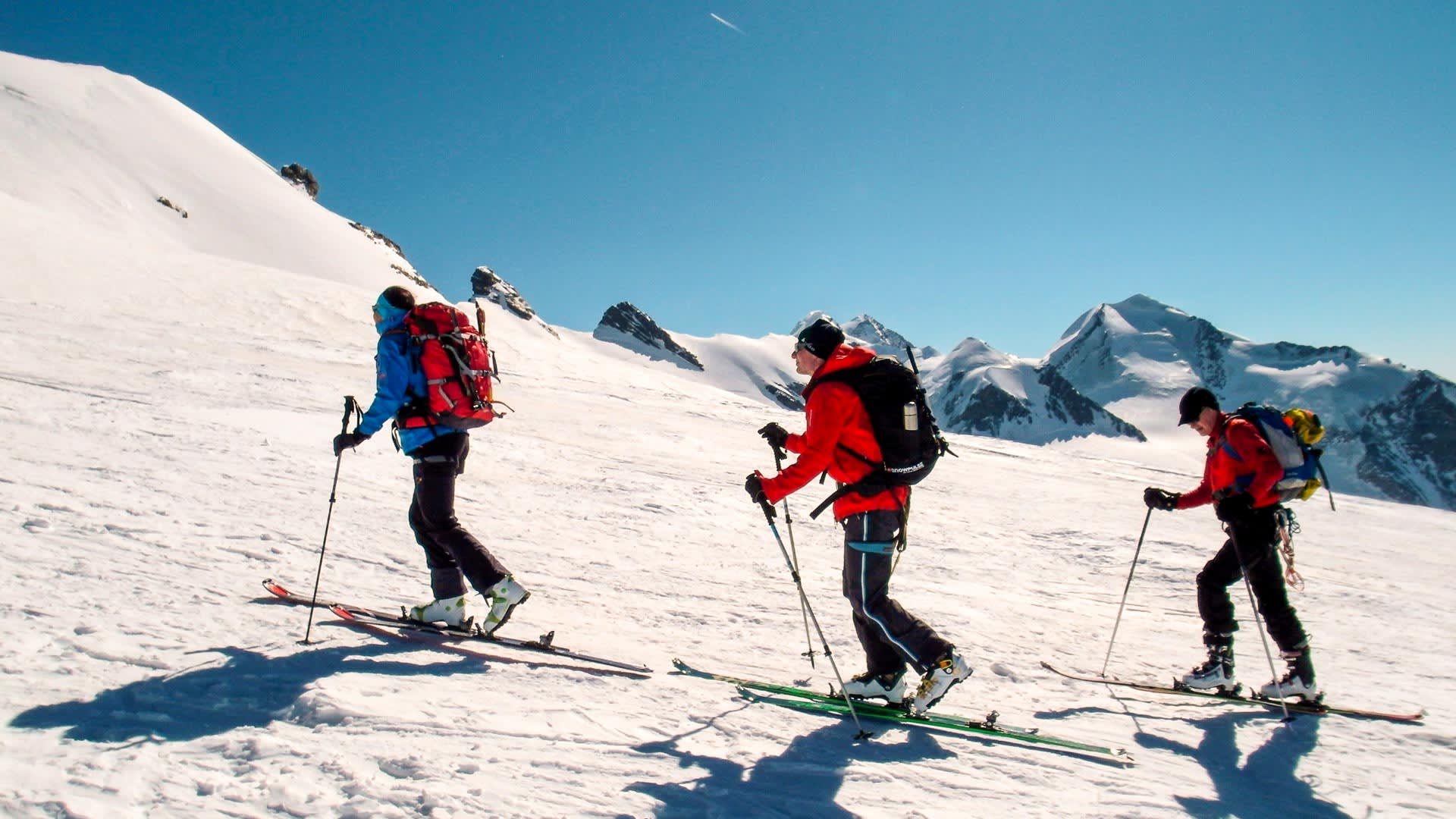 Drei Skitourengeher steigen mit Fellen am Breithorn im Wallis auf einem schneebedeckten Hang auf.