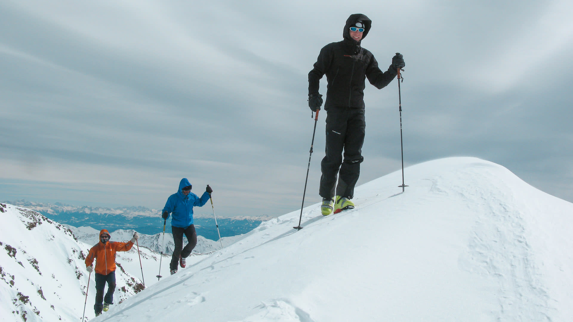 Drei Skitourengeher mit Fellen steigen auf einem Schneegrat Richtung Gipfel des Cevedale im Ortlergebiet auf.
