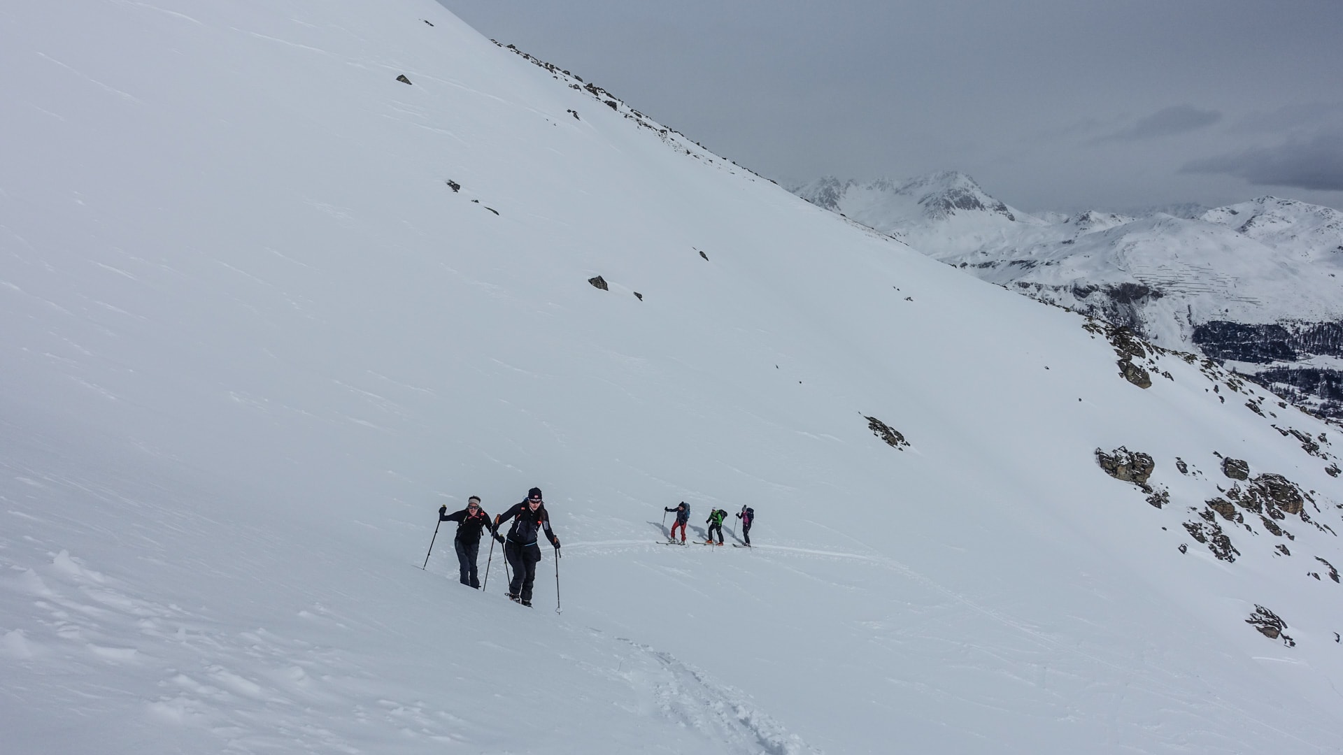 Fünf Skitourengeher mit Fellen und Rucksäcken steigen einen breiten Schneehang im Val Müstair auf.